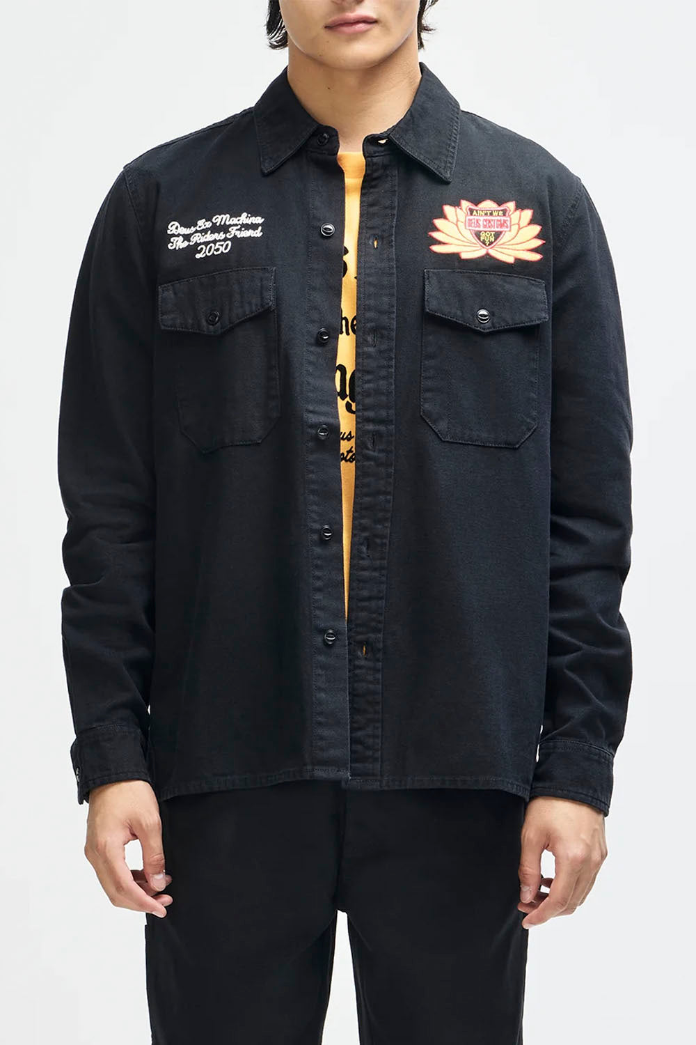 A model wearing a black denim button-up shirt jacket over a yellow t-shirt, featuring embroidered designs on the chest pockets.