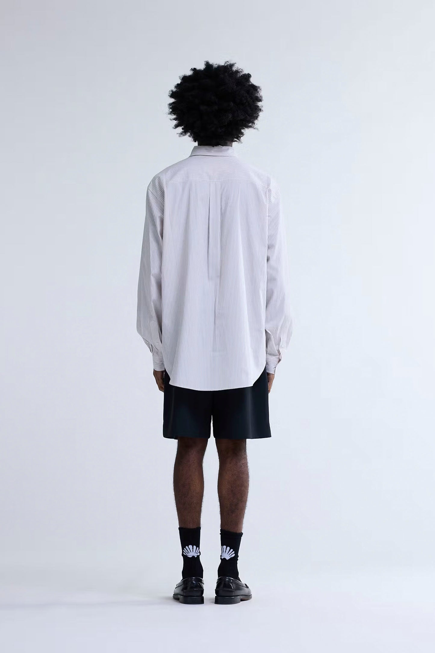 Person wearing New Amsterdam Surf Association Beach Shirt in Stripe shirt and black shorts on a white background