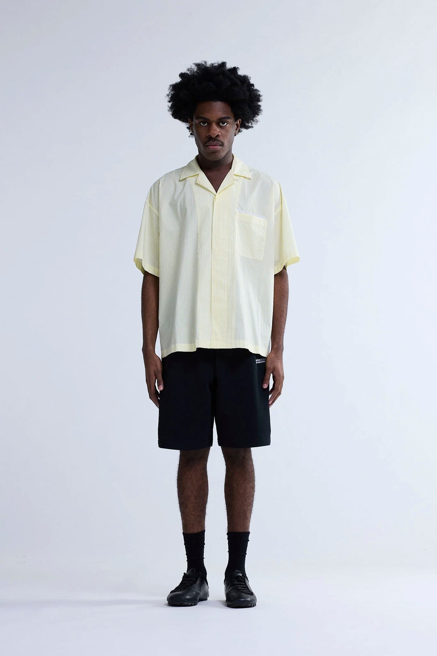 Person wearing New Amsterdam Surf Association Wijk Short Sleeved Shirt in Yellow Stripes and black shorts on a white background