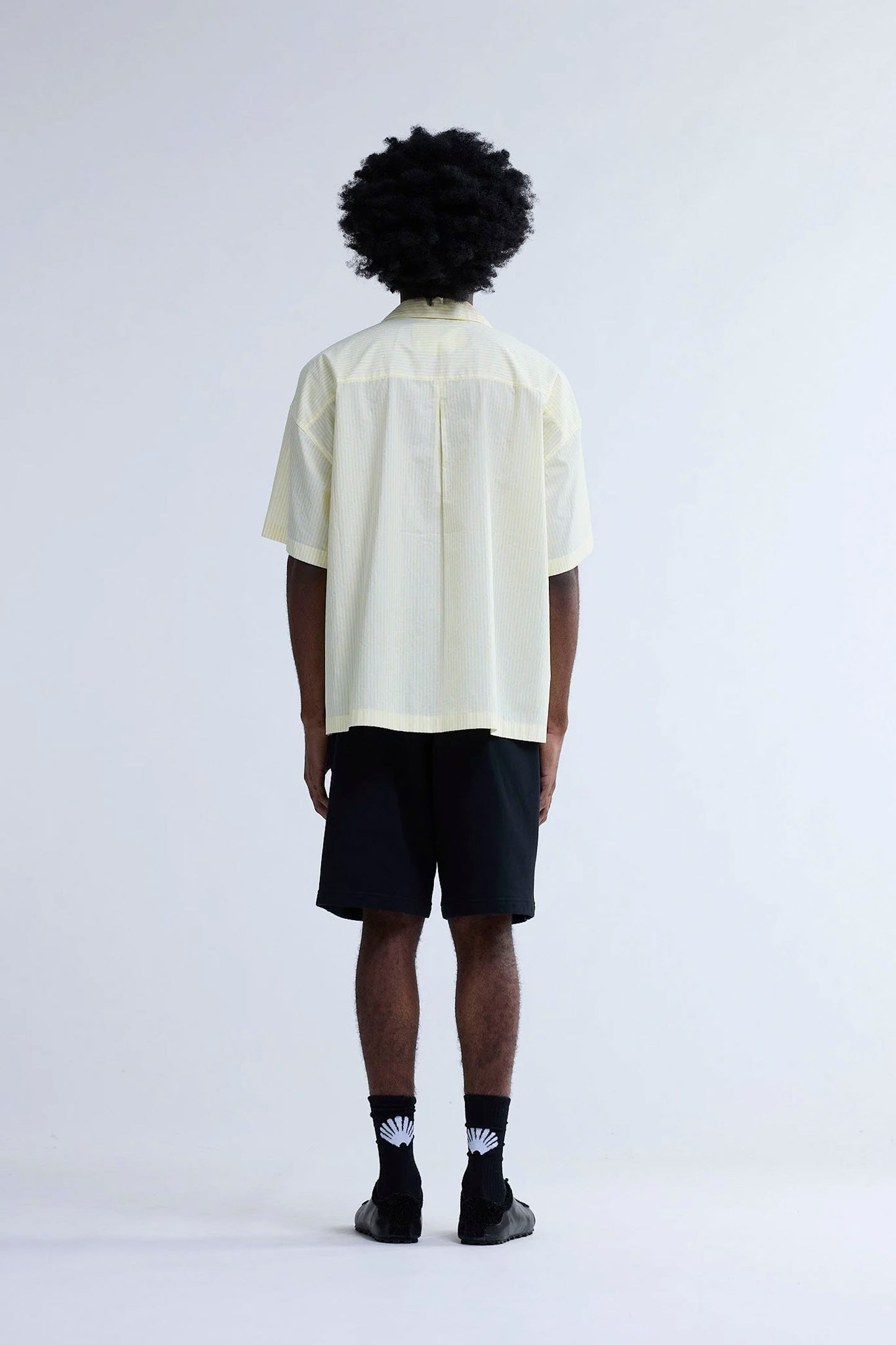 Person wearing New Amsterdam Surf Association Wijk Short Sleeved Shirt in Yellow Stripes and black shorts on a white background