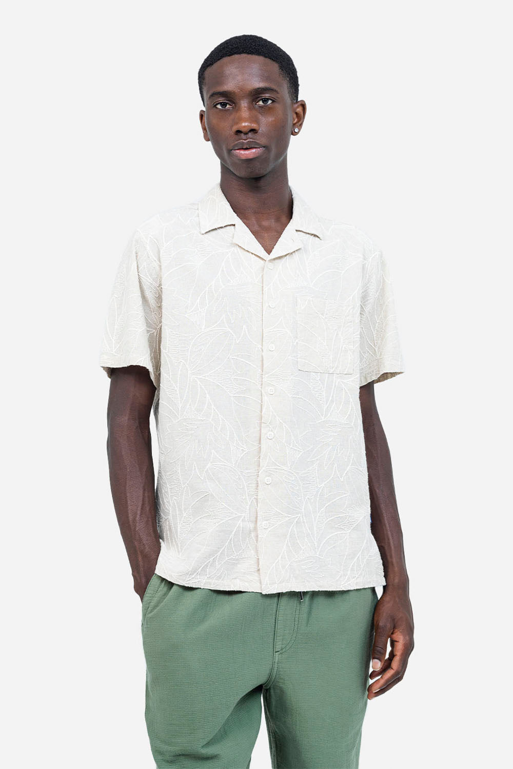 Man wearing a beige short-sleeve shirt and green pants on a white background