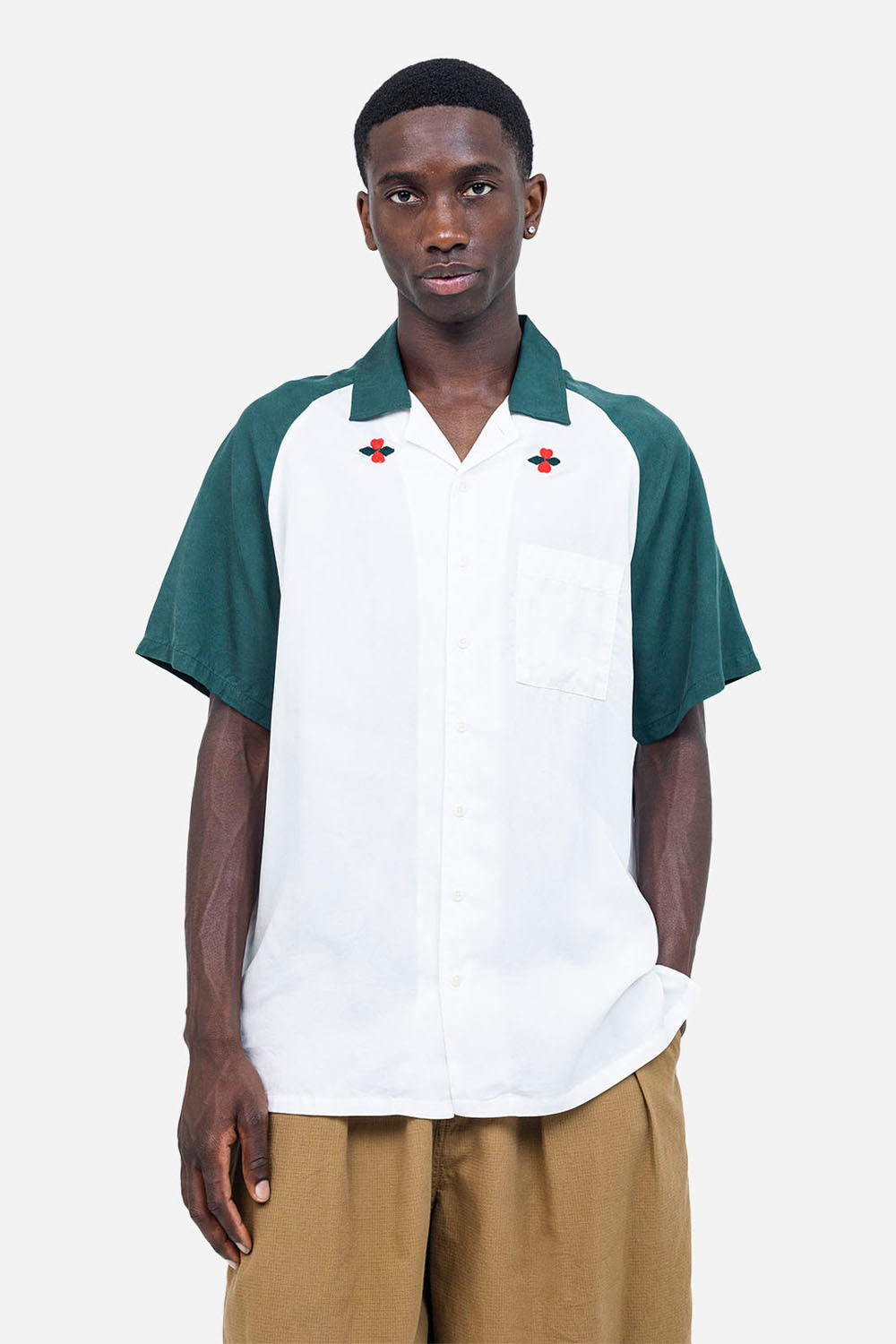 Man wearing a white shirt with green sleeves and a red emblem on a white background