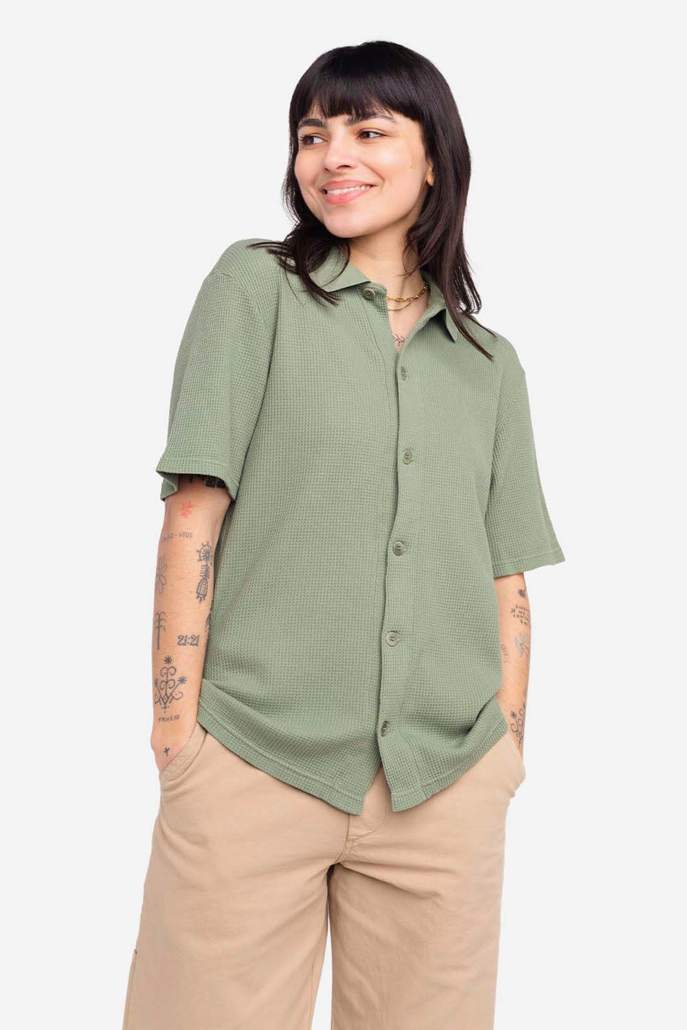 Woman wearing a green button-up shirt and beige pants on a white background