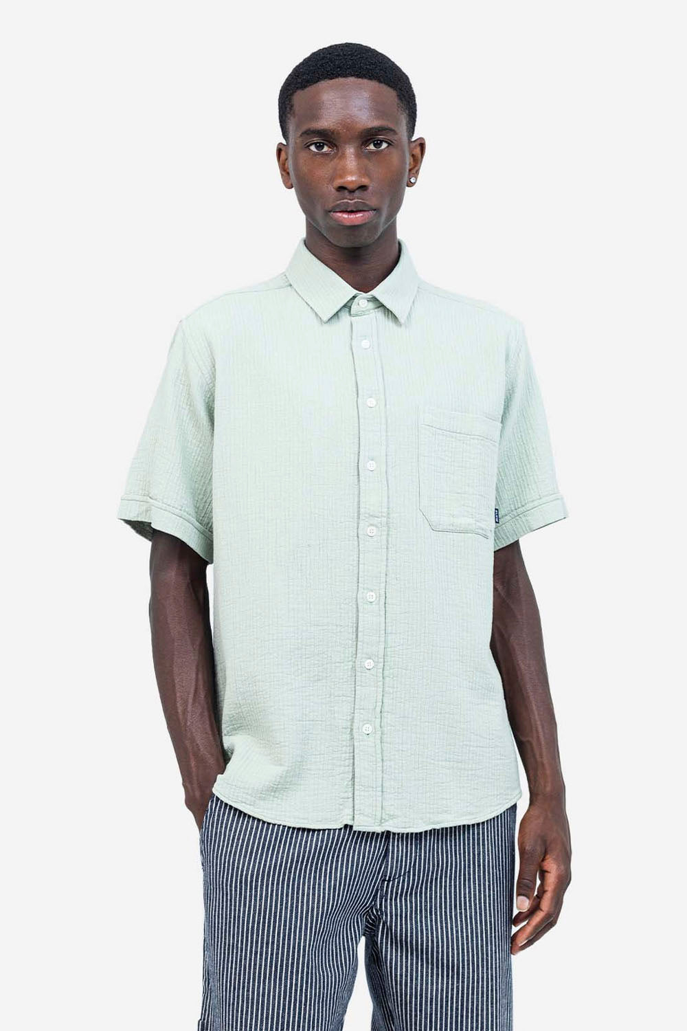 Man wearing a light green short-sleeve shirt and striped pants on a white background