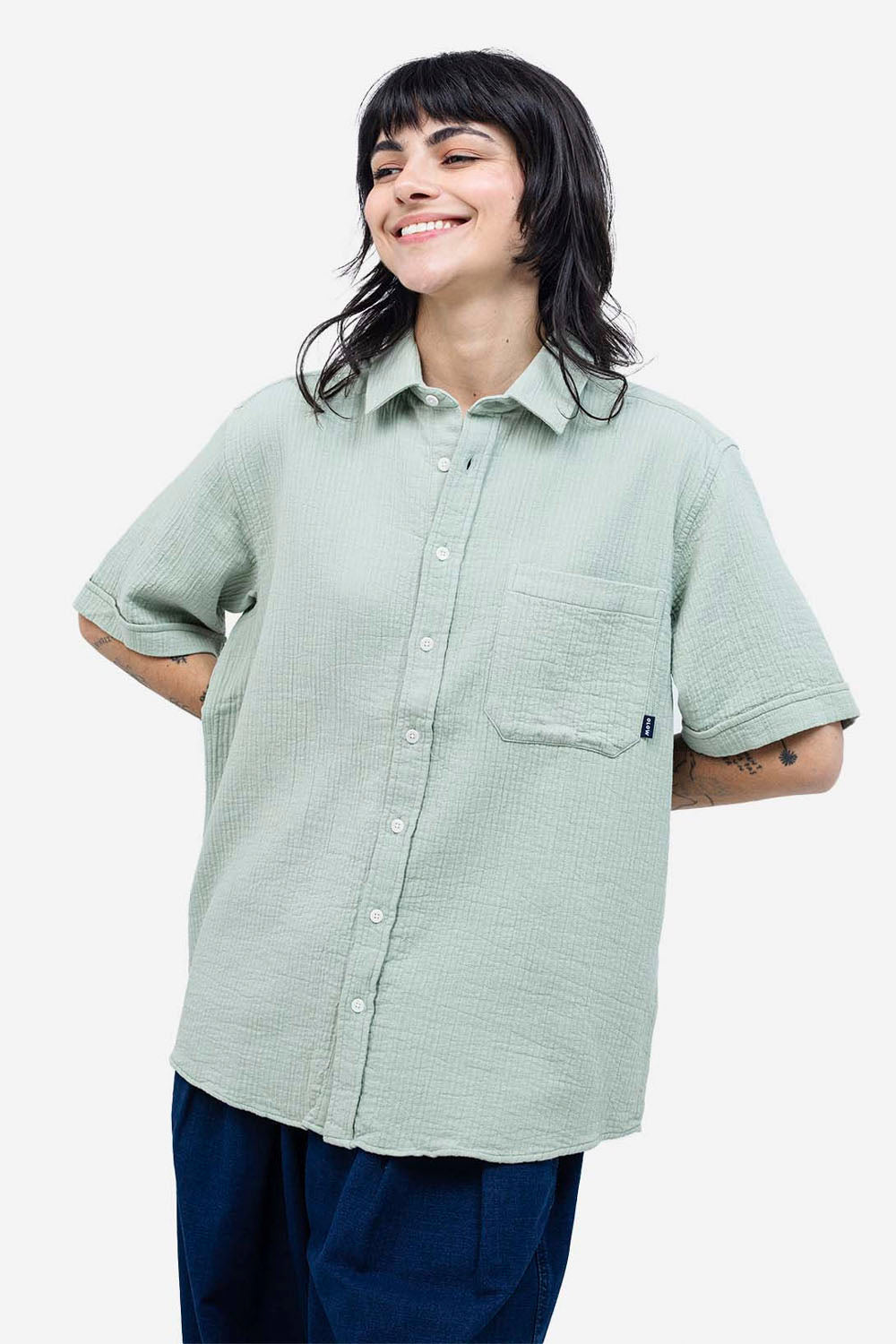 Person wearing a light green button-up shirt with short sleeves on a white background
