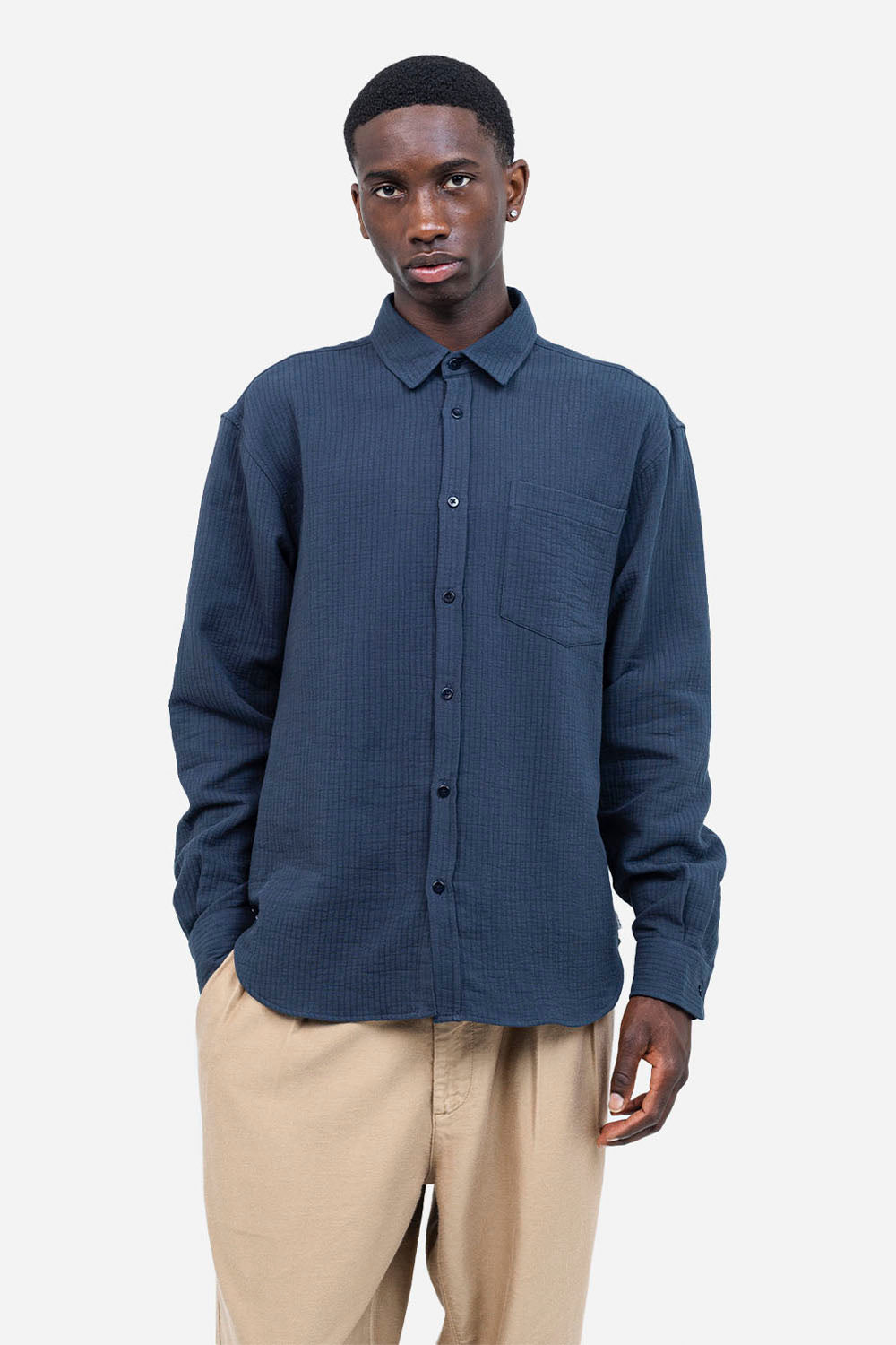 Man wearing a blue textured shirt and beige pants on a white background