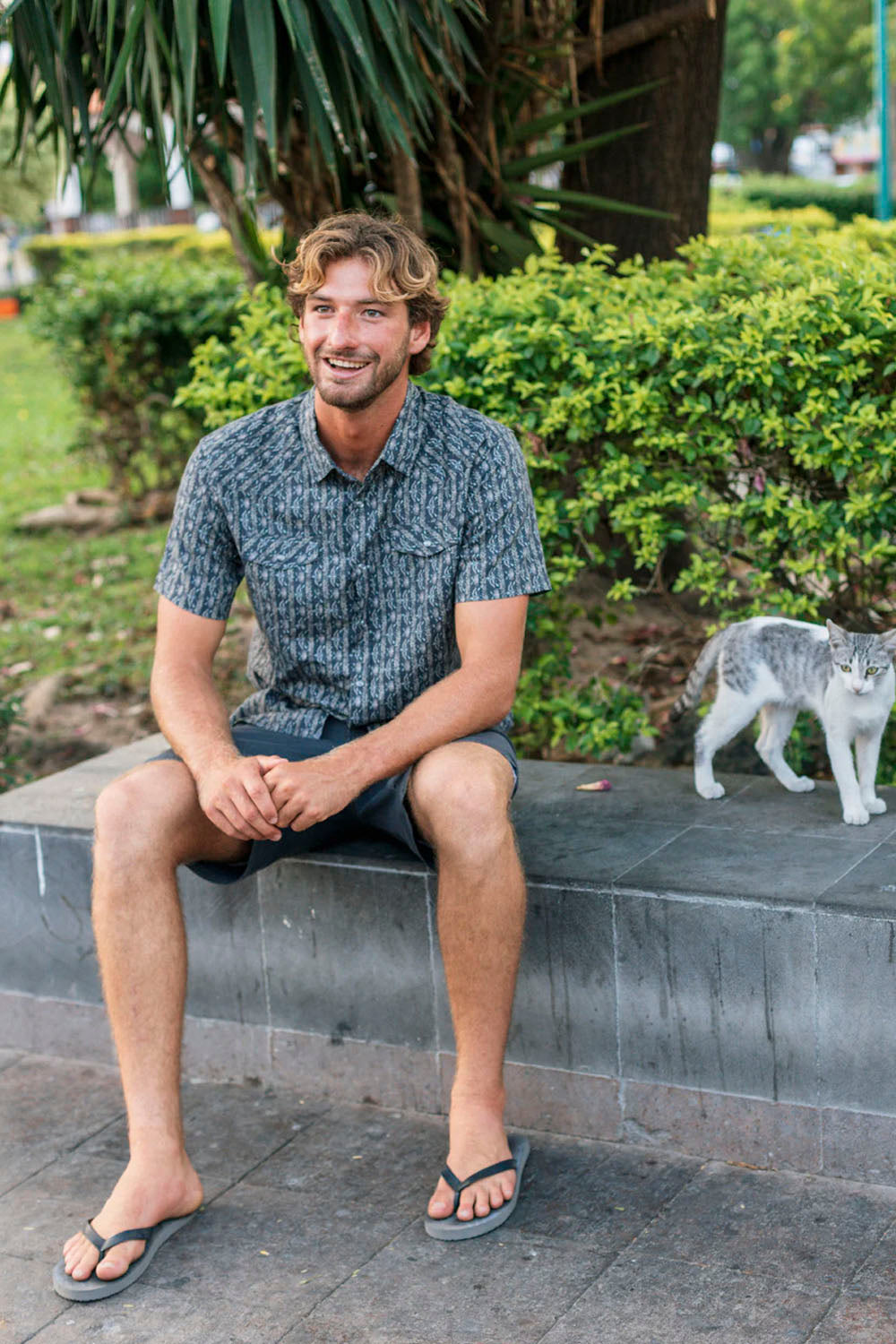 Man sitting on a stone bench with a cat in a park-like setting