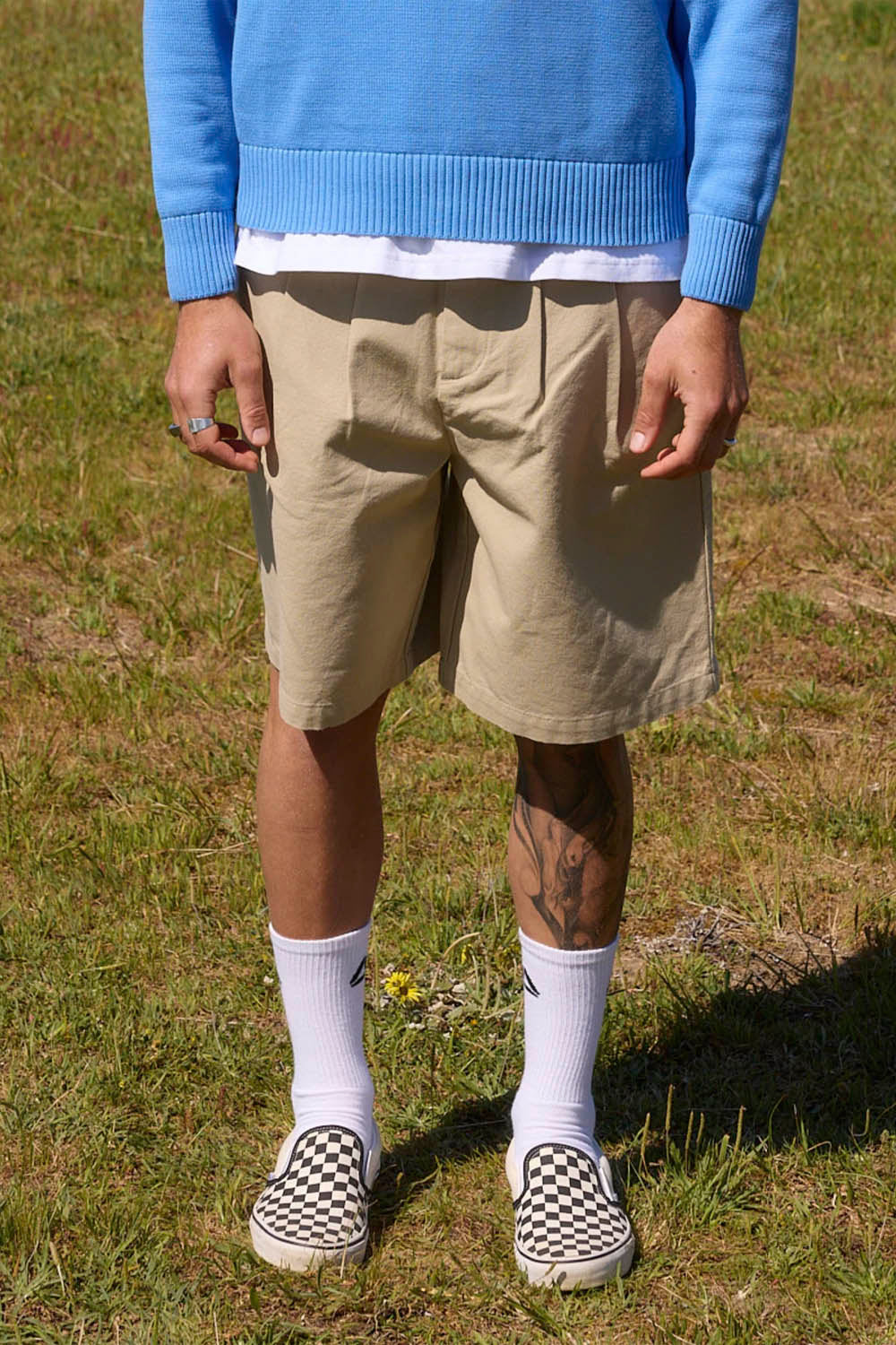 Person wearing a blue sweater, beige shorts, white socks, and checkered shoes on grass.