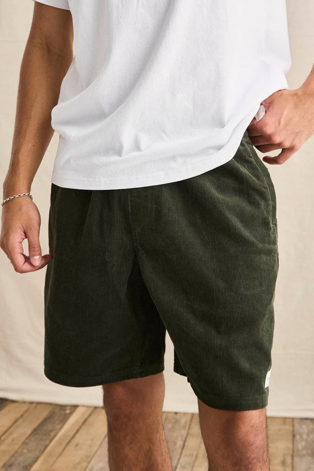 Person wearing green shorts and a white shirt against a neutral background