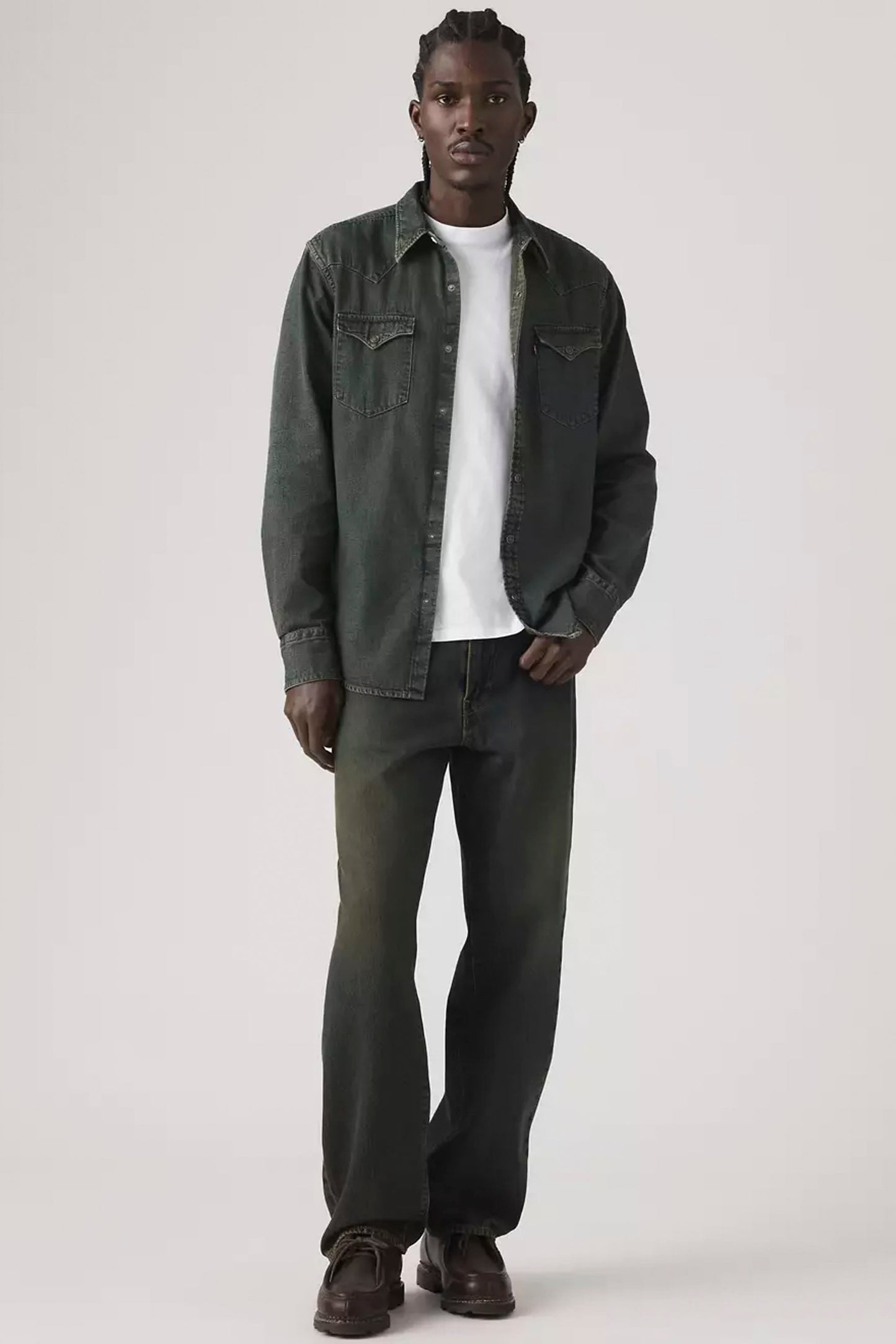 Man wearing a dark green denim jacket, white shirt, and dark jeans on a white background