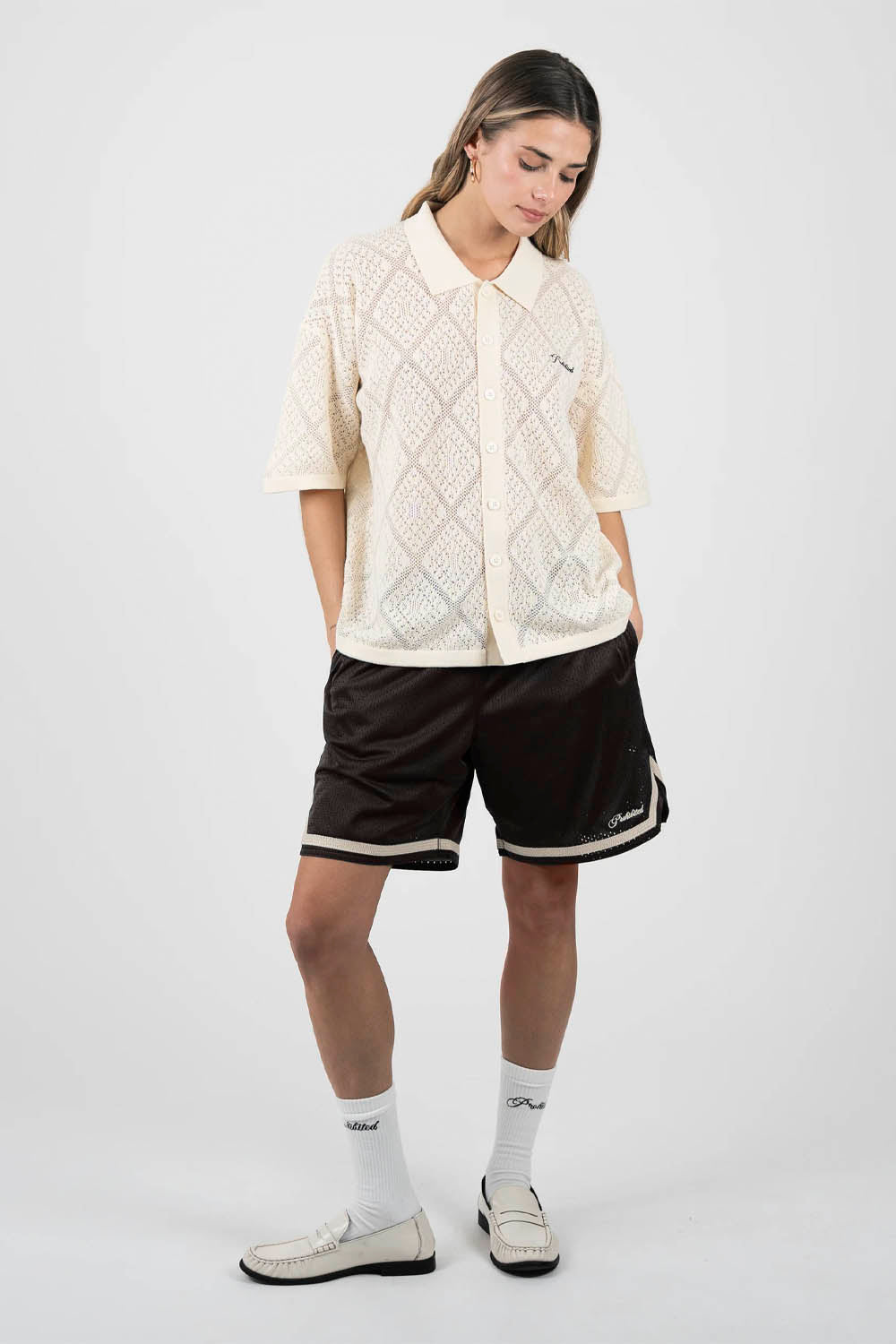 Person wearing a cream patterned shirt and black shorts on a white background