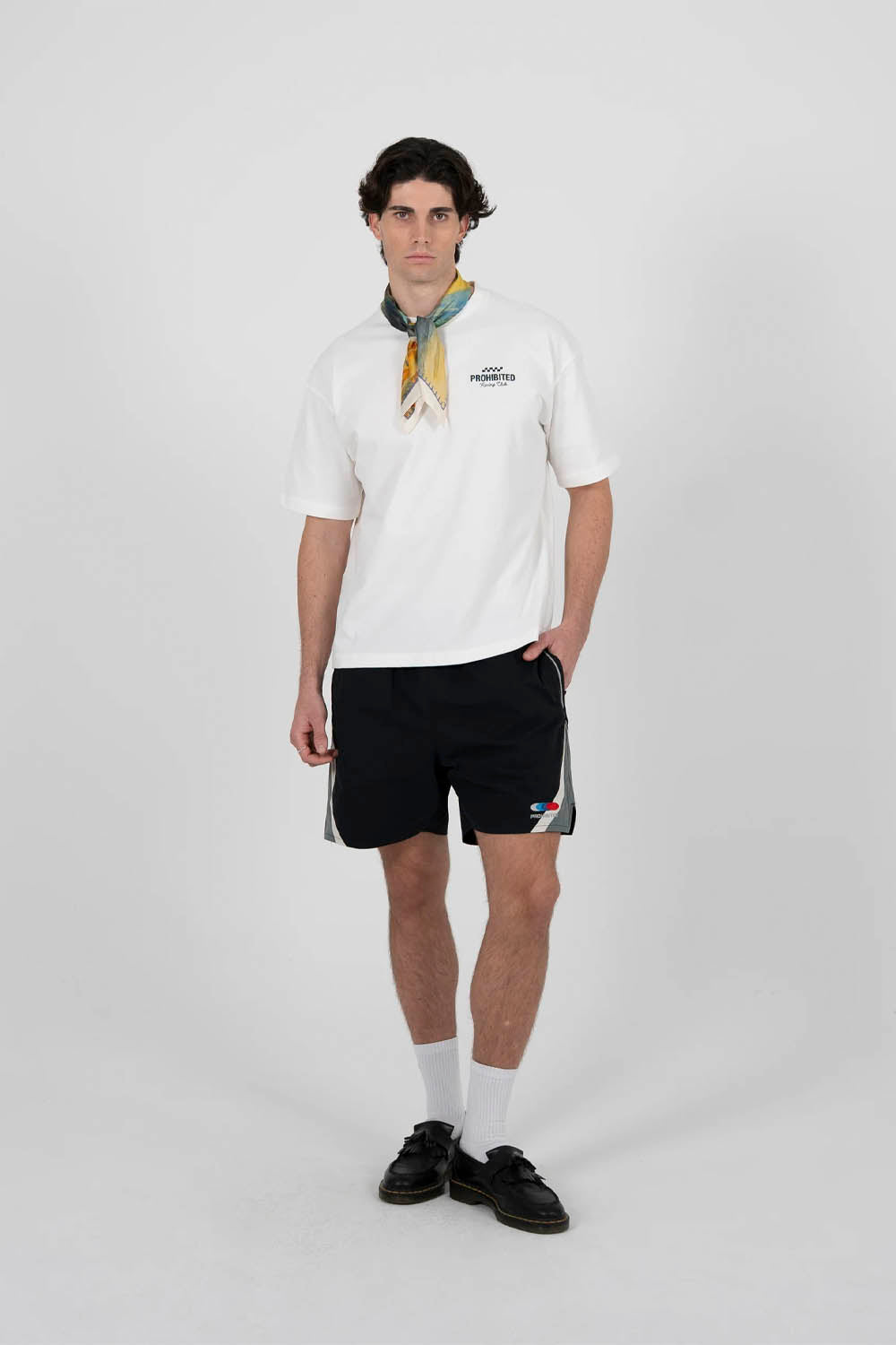 Person wearing a white polo shirt with a logo, black shorts, and a yellow scarf on a white background