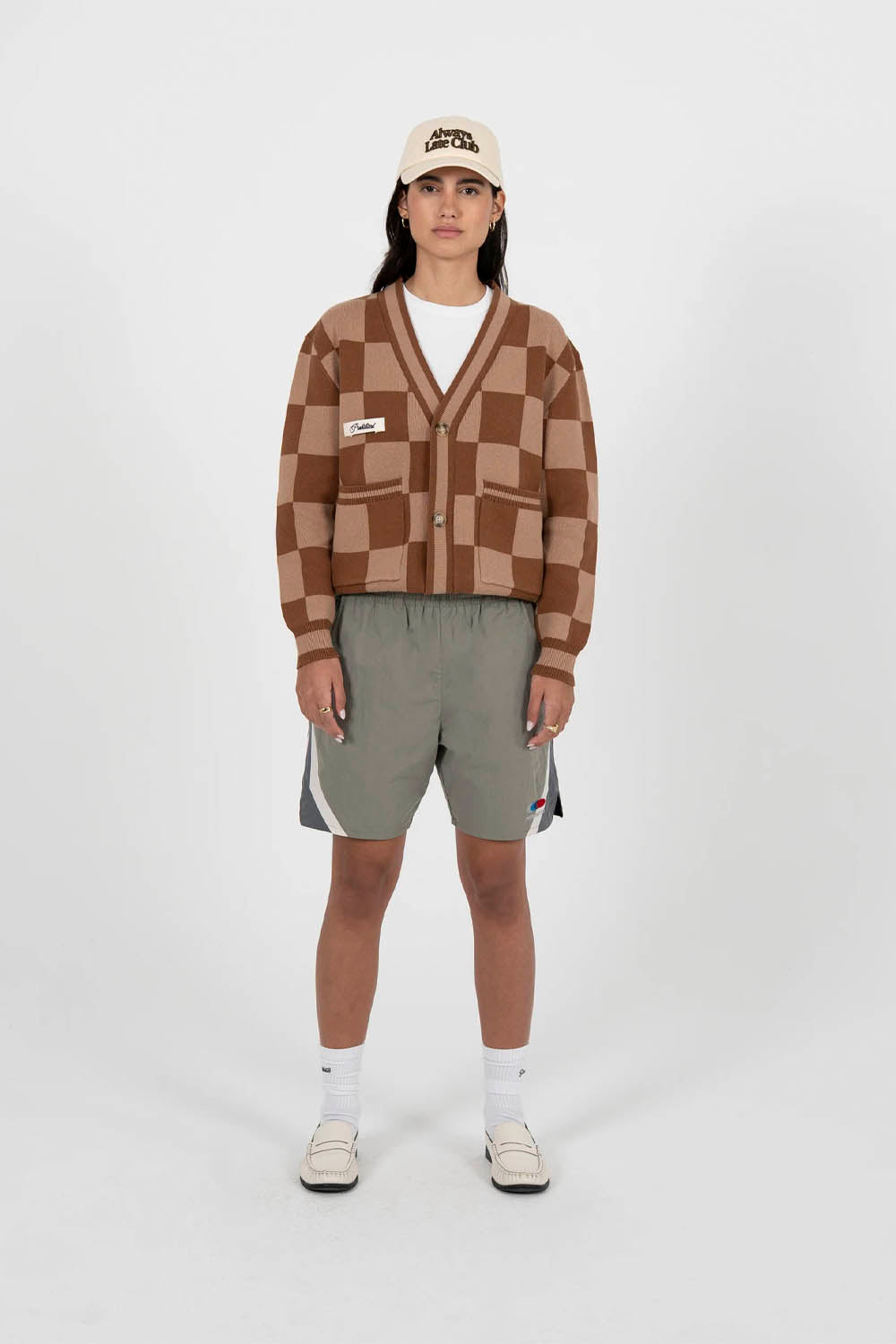 Person wearing a checkered sweater, shorts, and a cap on a white background