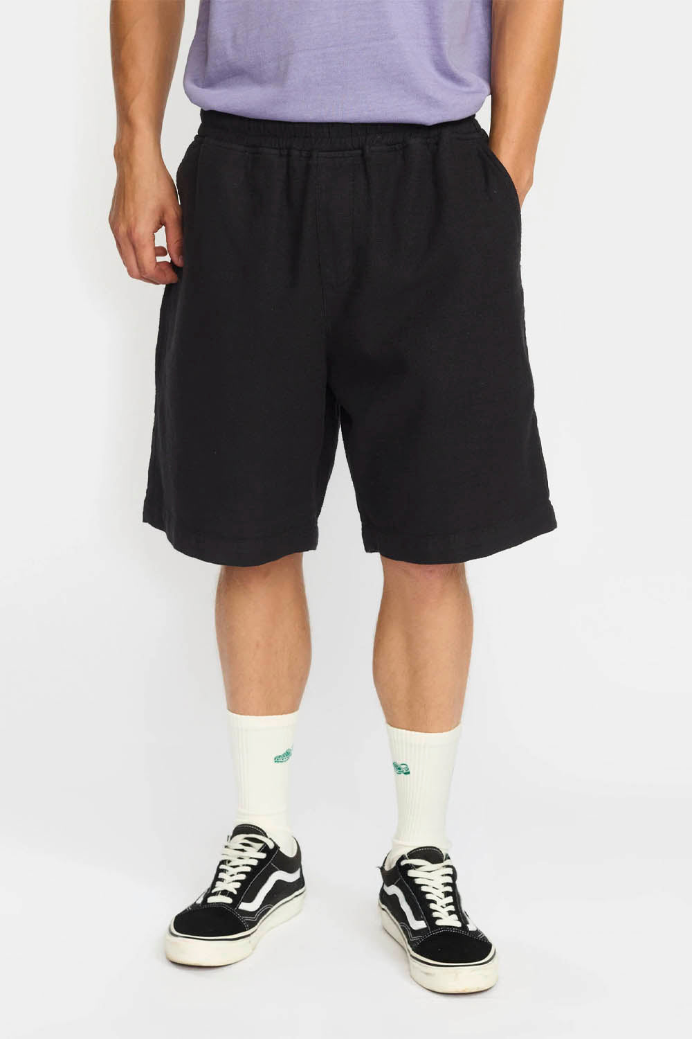 Person wearing black shorts, a light purple shirt, and black sneakers on a white background
