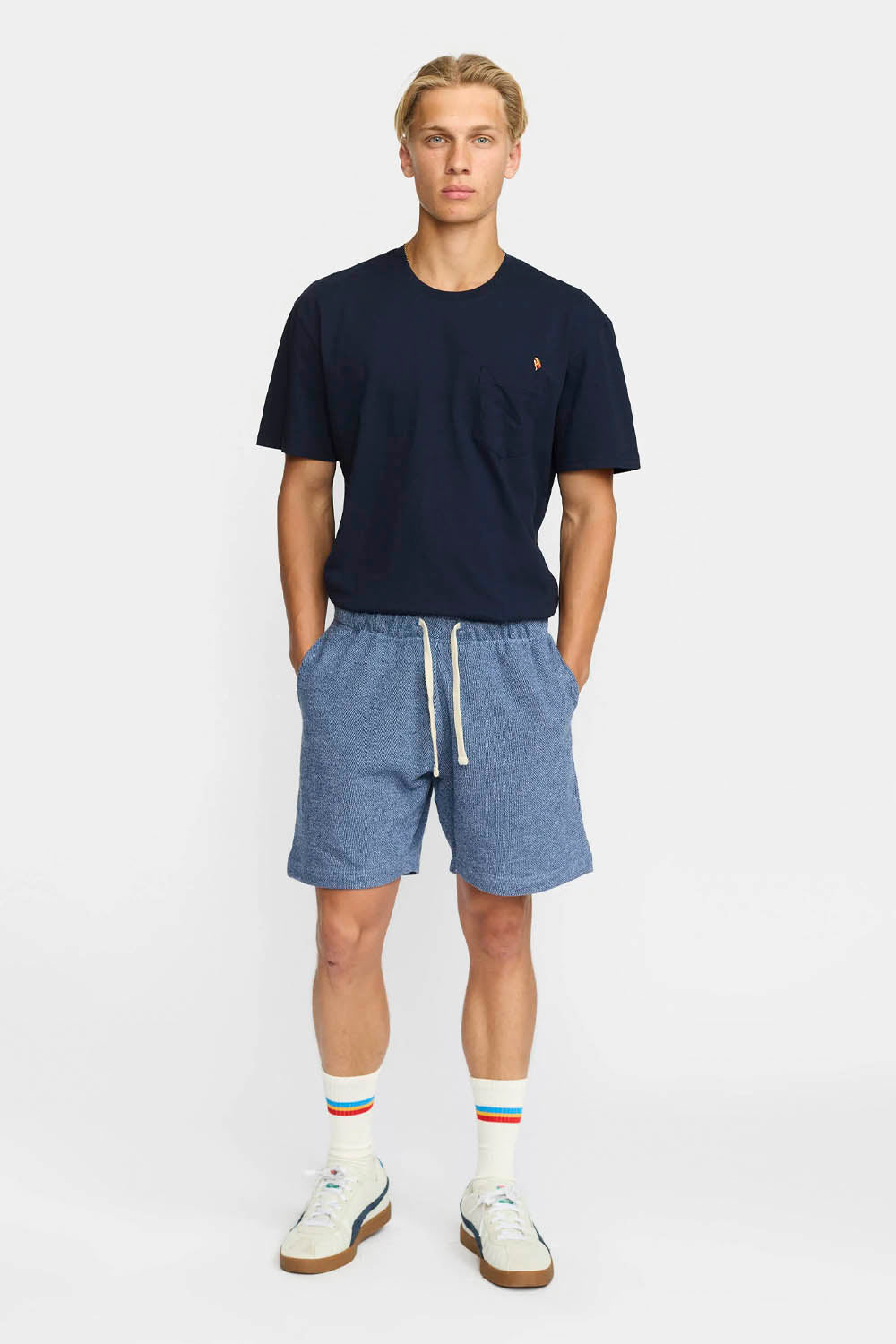 Man wearing a navy t-shirt and blue shorts on a white background