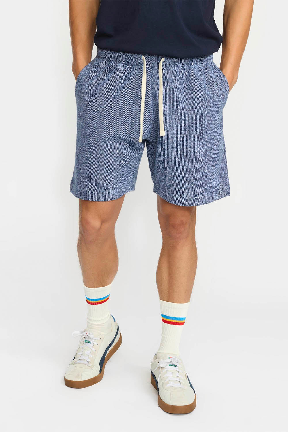 Person wearing blue shorts with a white drawstring, white socks with colorful stripes, and white sneakers on a plain background.