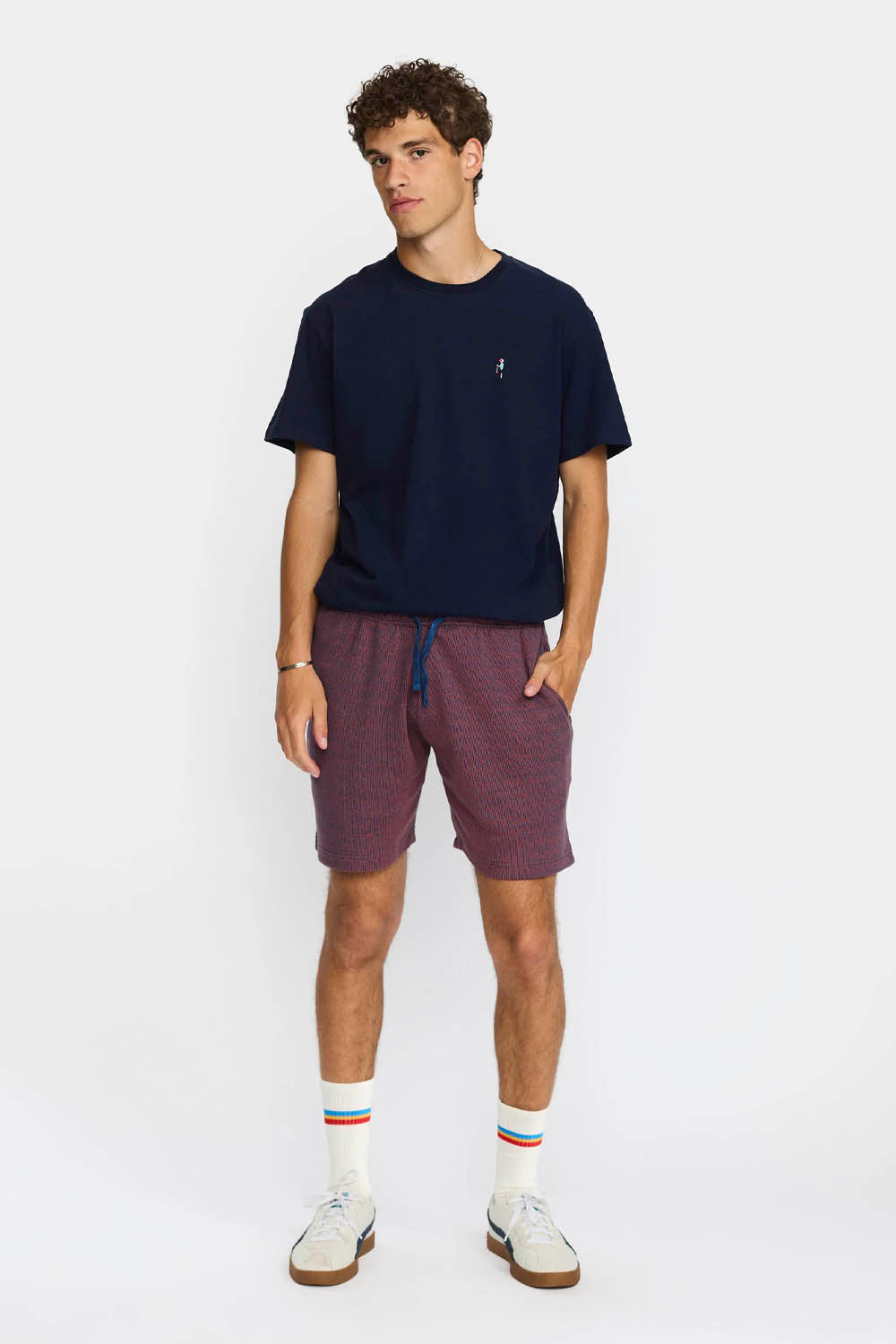 Person wearing navy Revolution Jacquard shorts, white socks with colorful stripes, and white sneakers on a white background