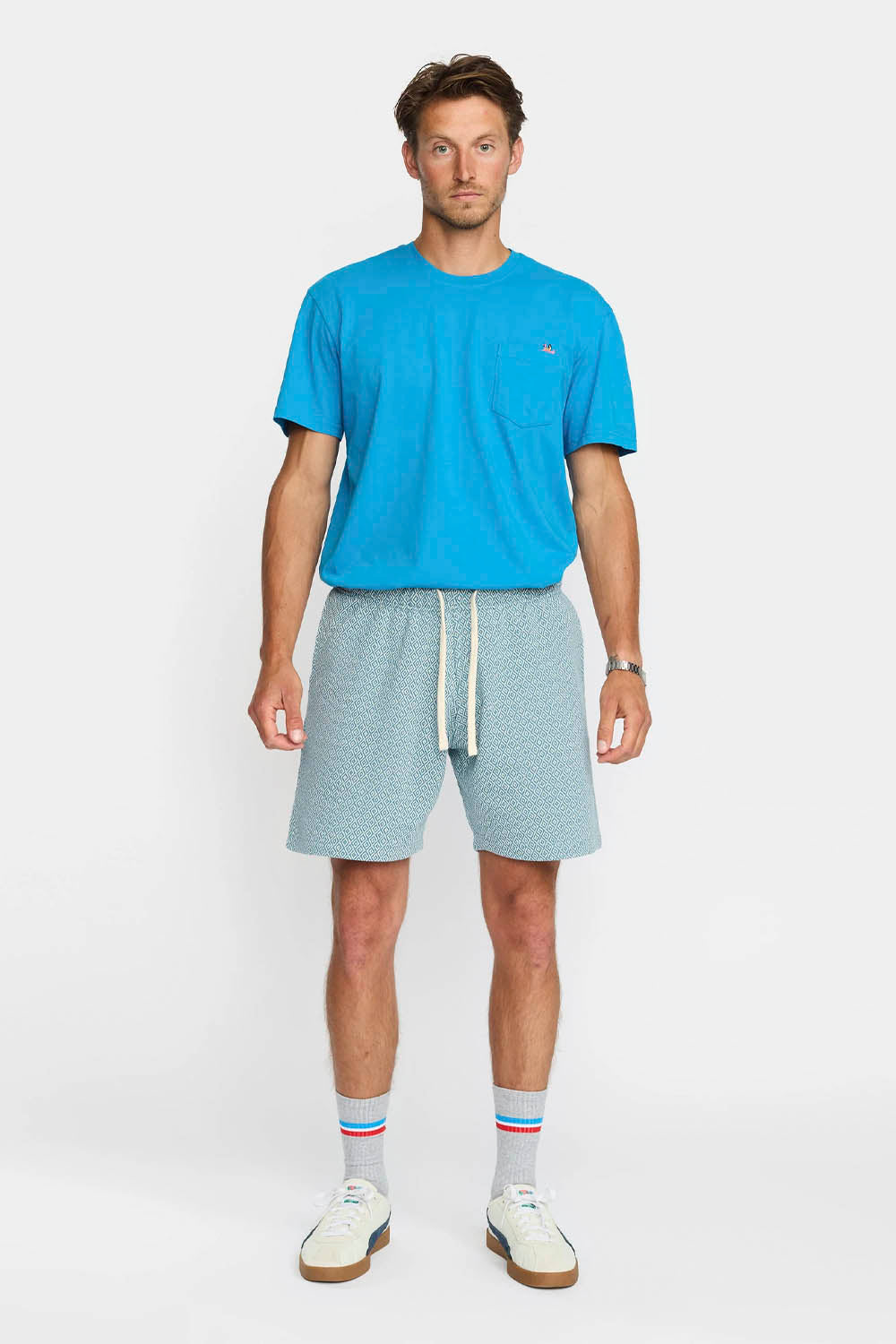 Man wearing a blue t-shirt and light gray shorts on a white background