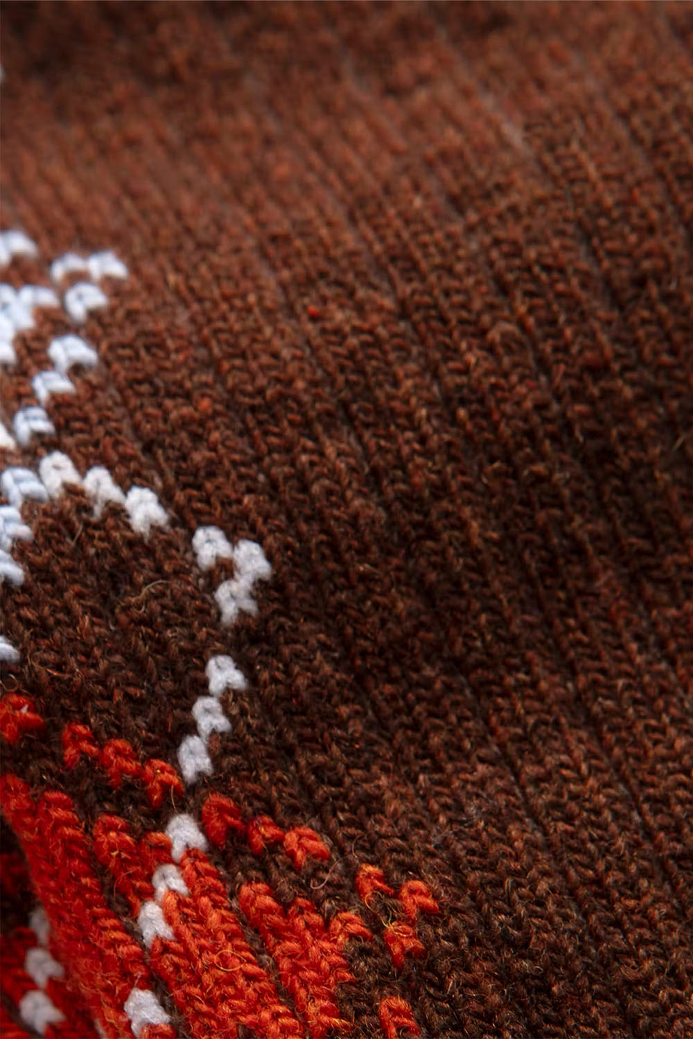 Close-up of a brown knit textile with a white and orange patterned design, showing the texture of the yarn.
