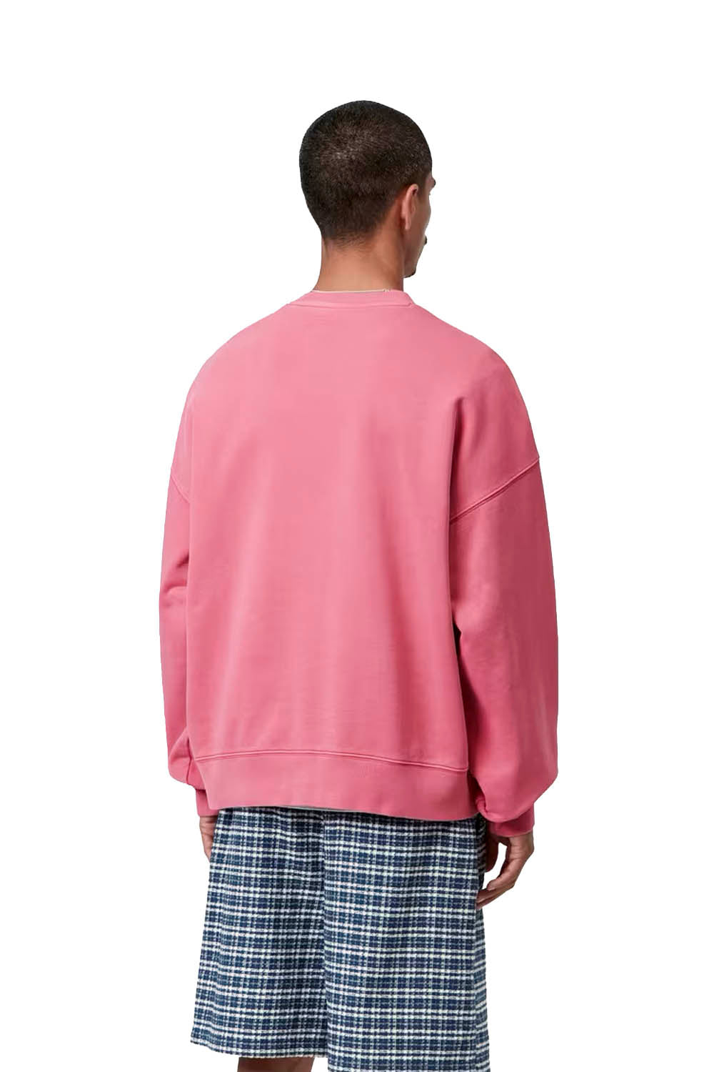 Person wearing a pink sweatshirt and plaid shorts on a white background