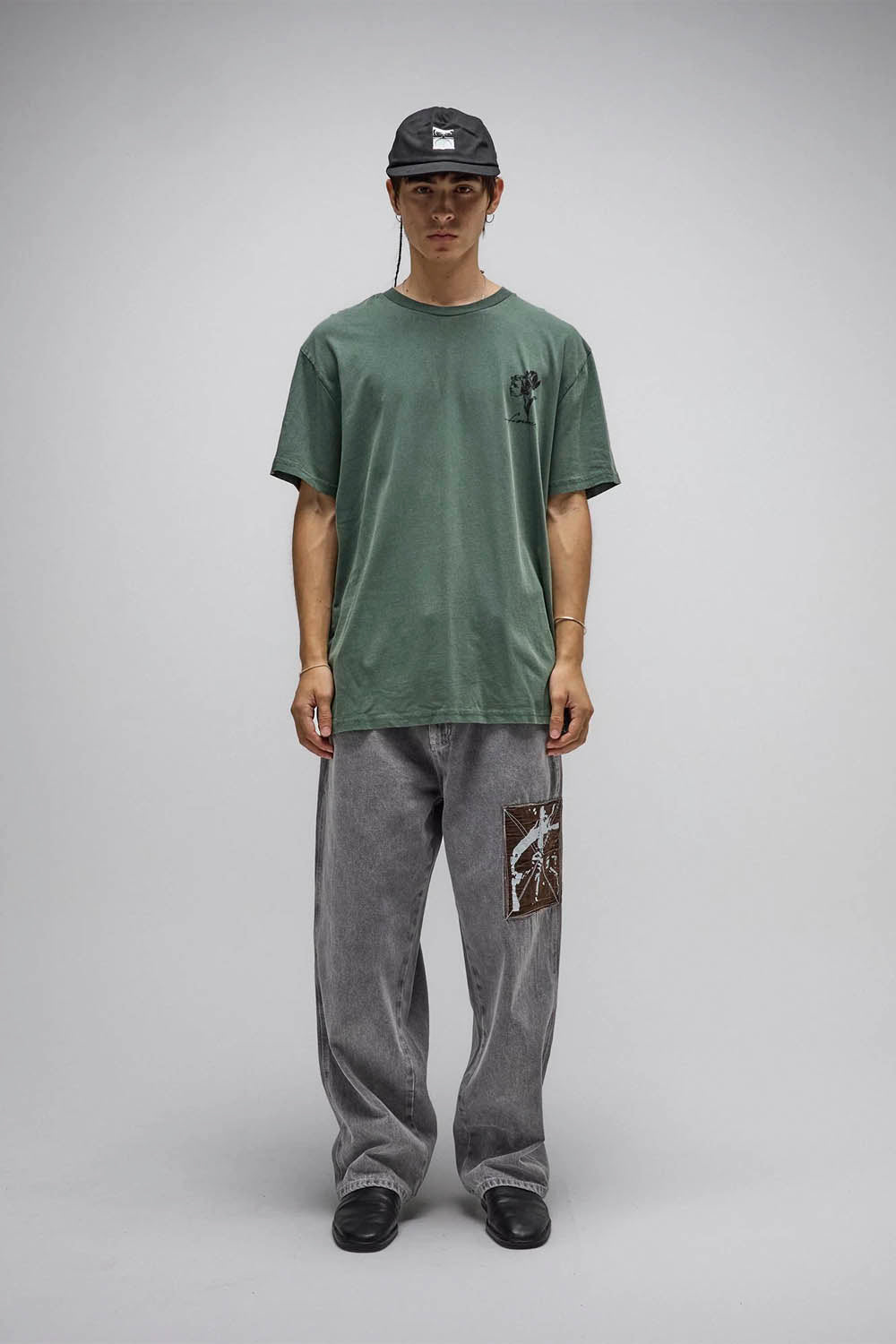 Person wearing a green t-shirt and gray pants with a logo on a gray background