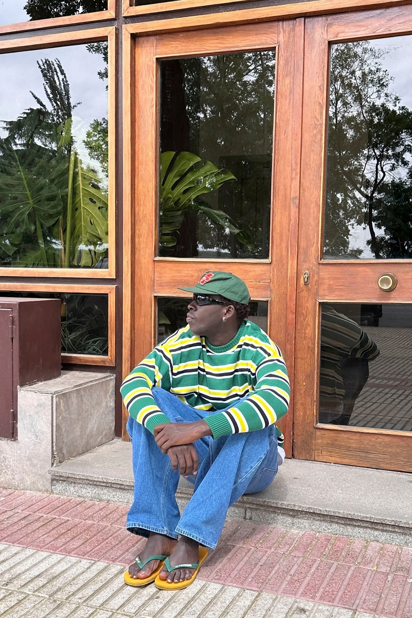 Man sitting on a step in front of a building with Nowhere striped sweater Pukas Surf Shop
