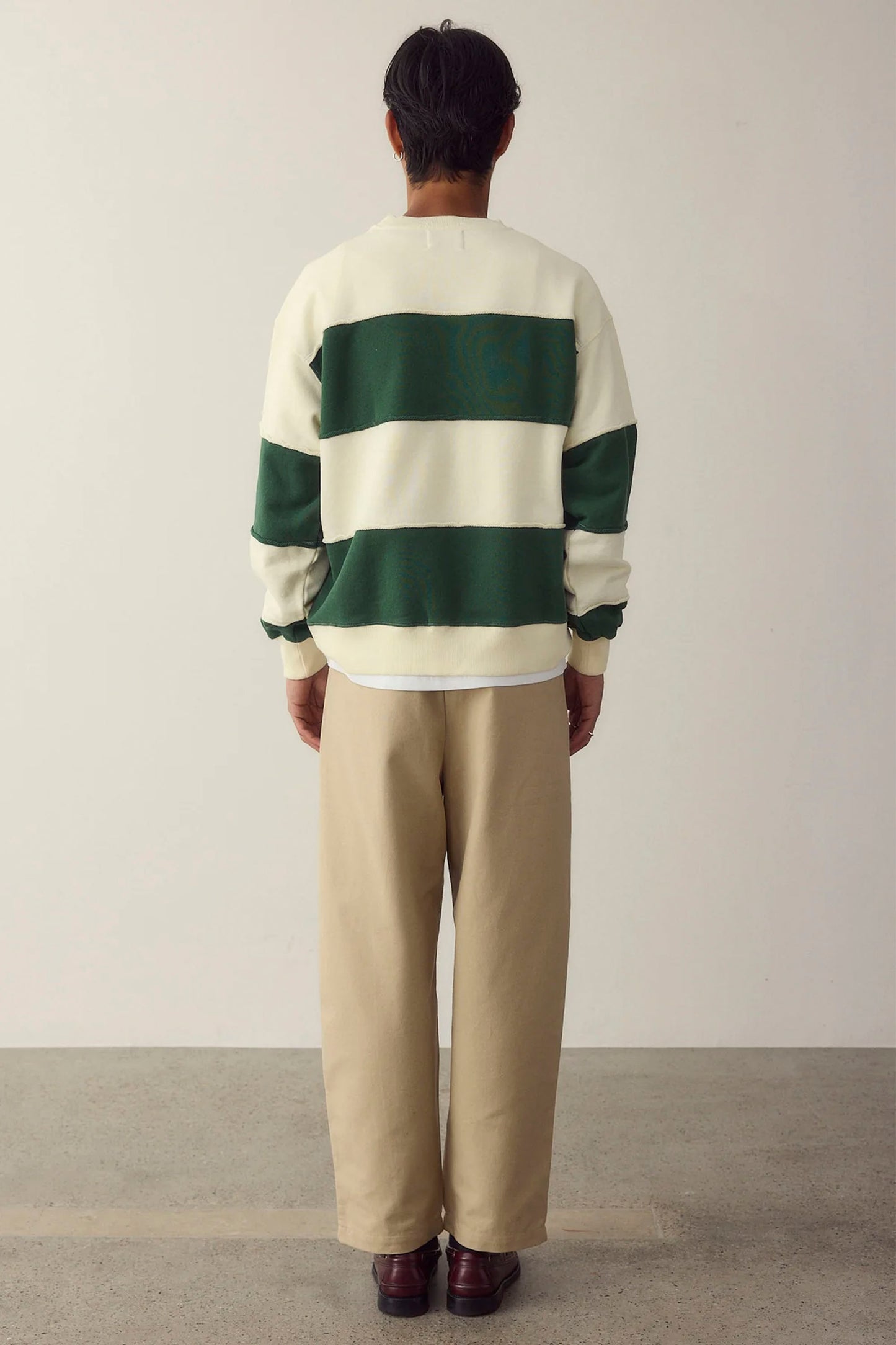 Person wearing a green and white striped NWHR sweater with beige pants against a plain background