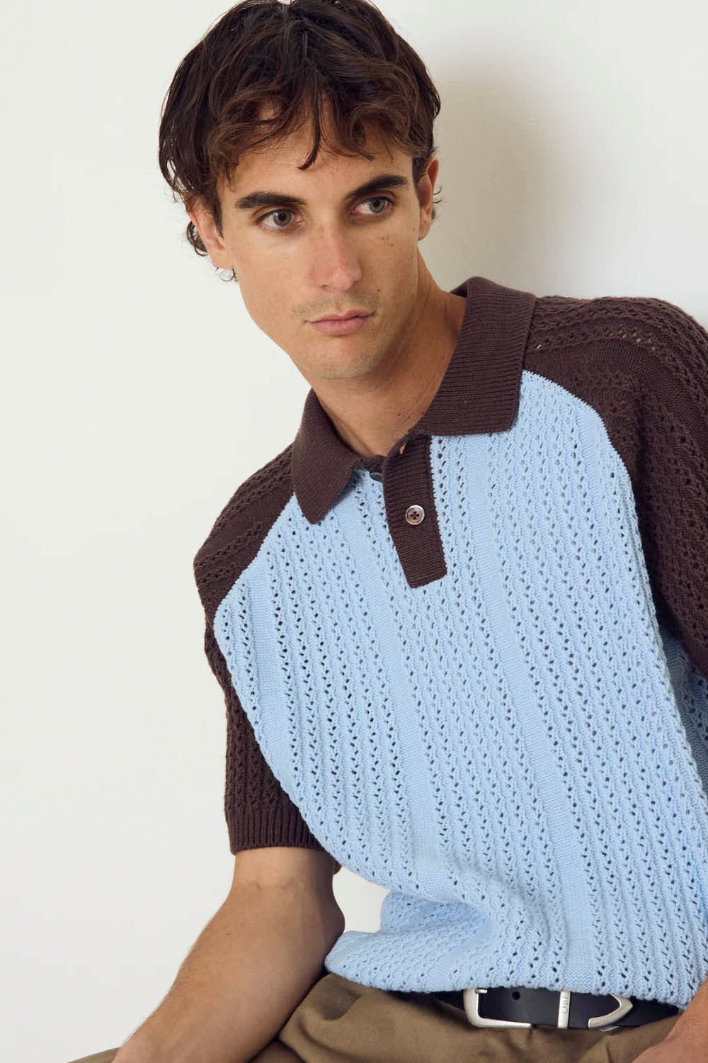 Man wearing a brown and blue knitted sweater over a white shirt against a plain background
