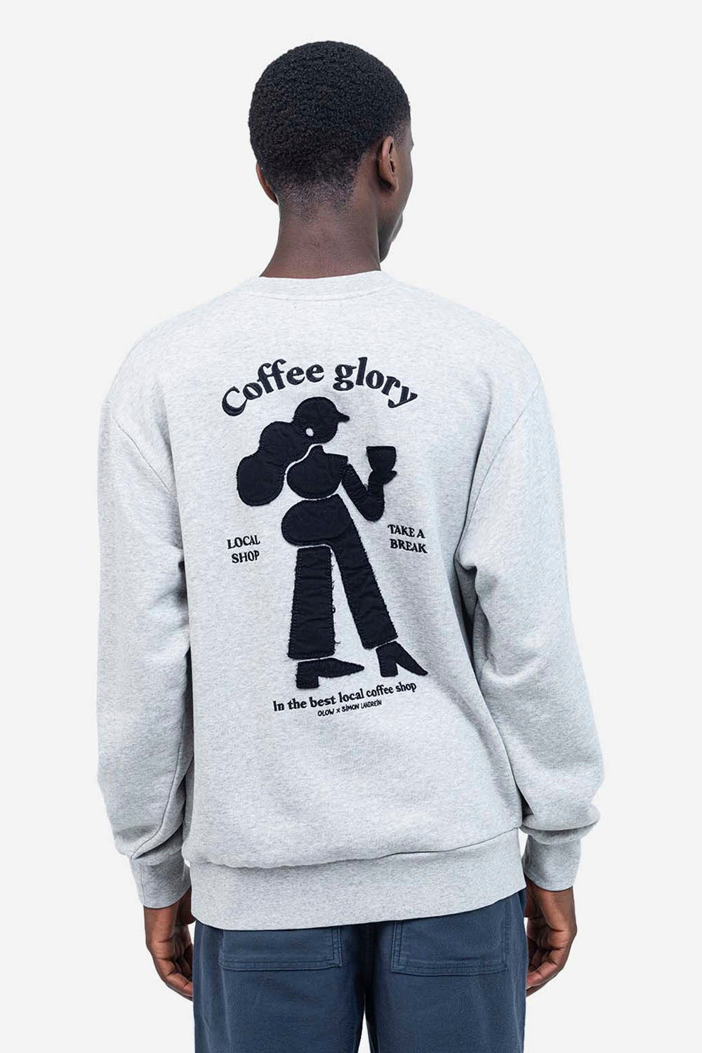 Person wearing a gray sweatshirt with a graphic and text on the back, standing against a white background