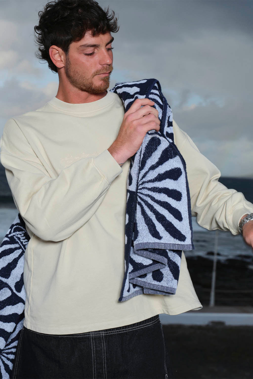 Man holding a patterned towel against a cloudy sky