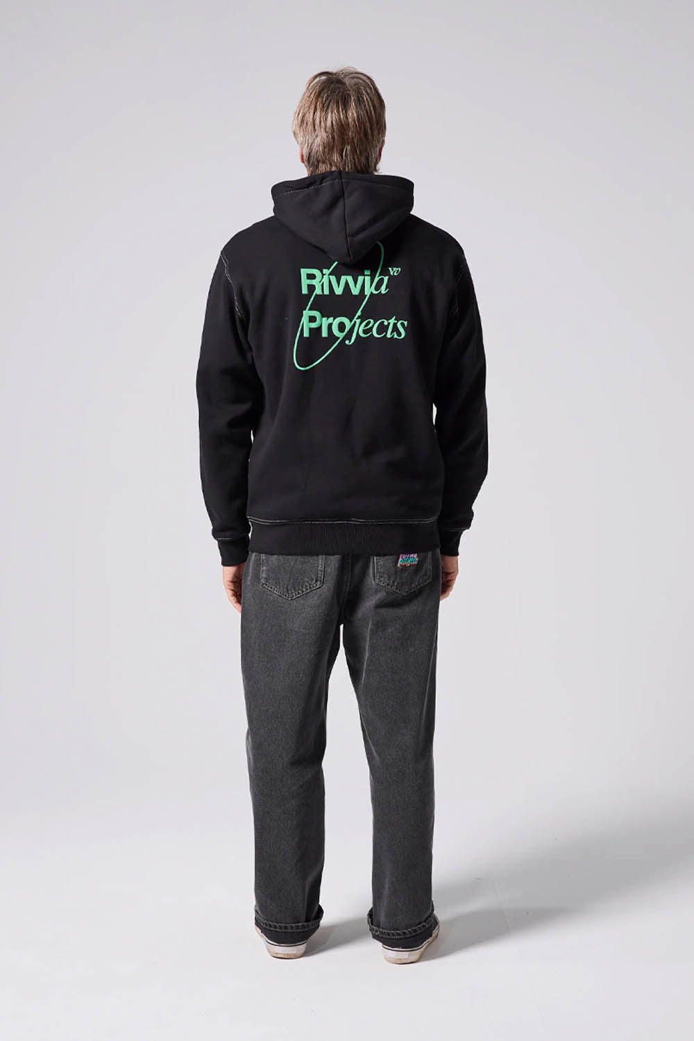 Person wearing a black hoodie with 'Rivvia Projects' logo on the back, standing against a white background