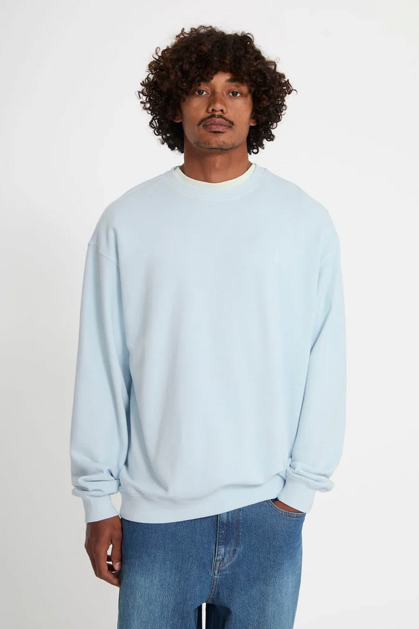 Man wearing a light blue Volcom Single Stone sweatshirt and jeans on a white background
