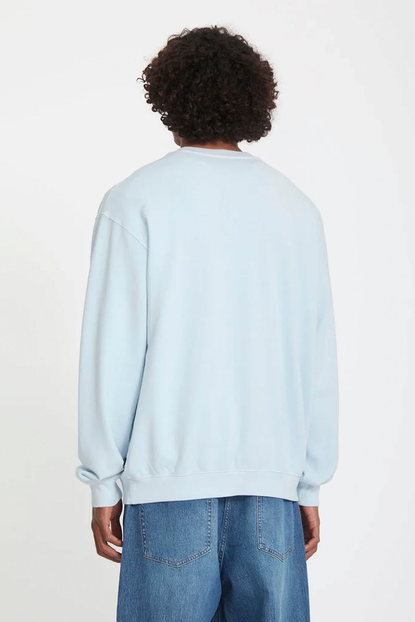 Person wearing a light blue Volcom Single Stone sweatshirt and blue jeans on a white background
