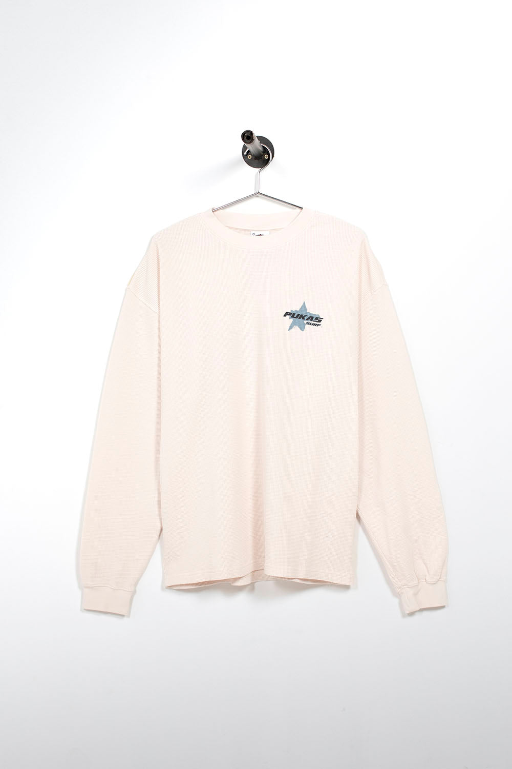A cream-colored long-sleeve crewneck sweatshirt hanging on a metal hanger against a white wall. The sweatshirt features a small graphic on the left chest depicting a blue star with the text 'HARPOON' in white.