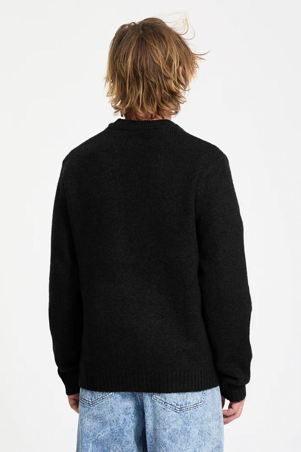 A person shown from the back wearing a black knit sweater and light blue jeans against a plain white studio background.