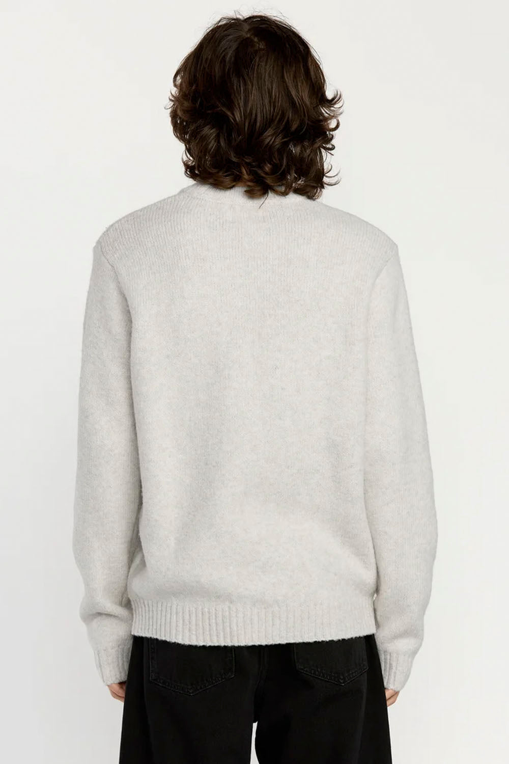 A person shown from the back wearing a light heather gray knit sweater and black pants against a plain light background.