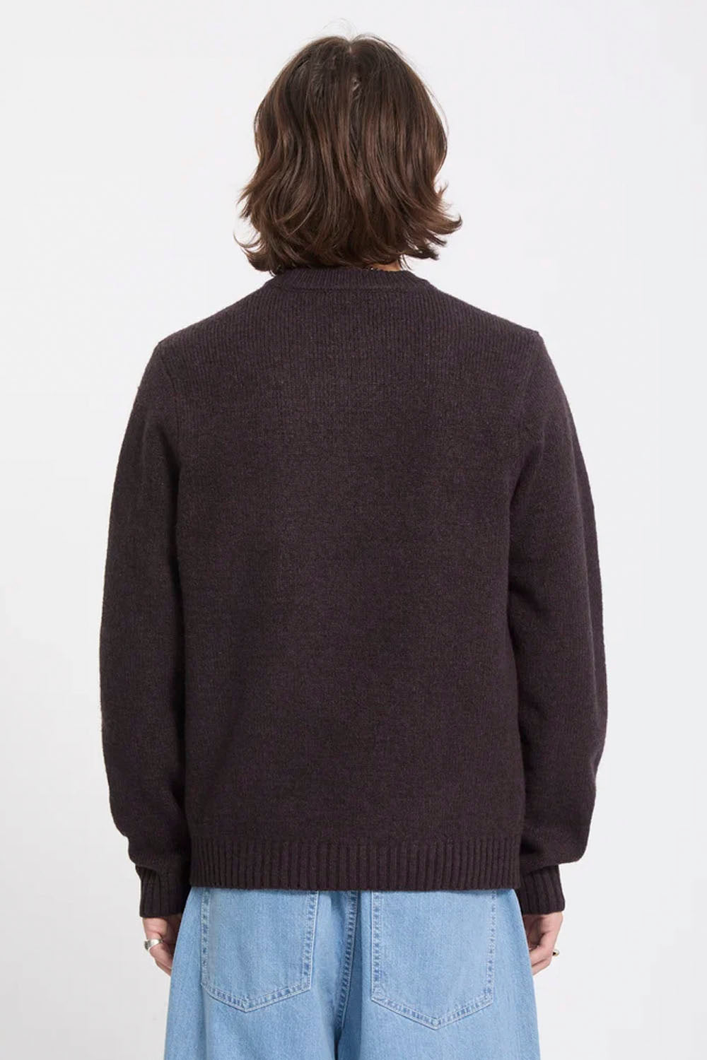 A person shown from the back wearing a dark brown ribbed knit sweater and light blue jeans against a plain white studio background.