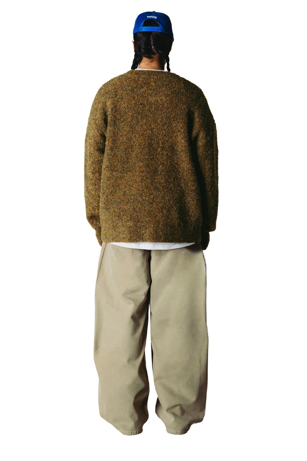A person shown from the back wearing a textured brown and beige knit sweater, loose beige pants, a white undershirt, and a blue baseball cap against a plain white background.