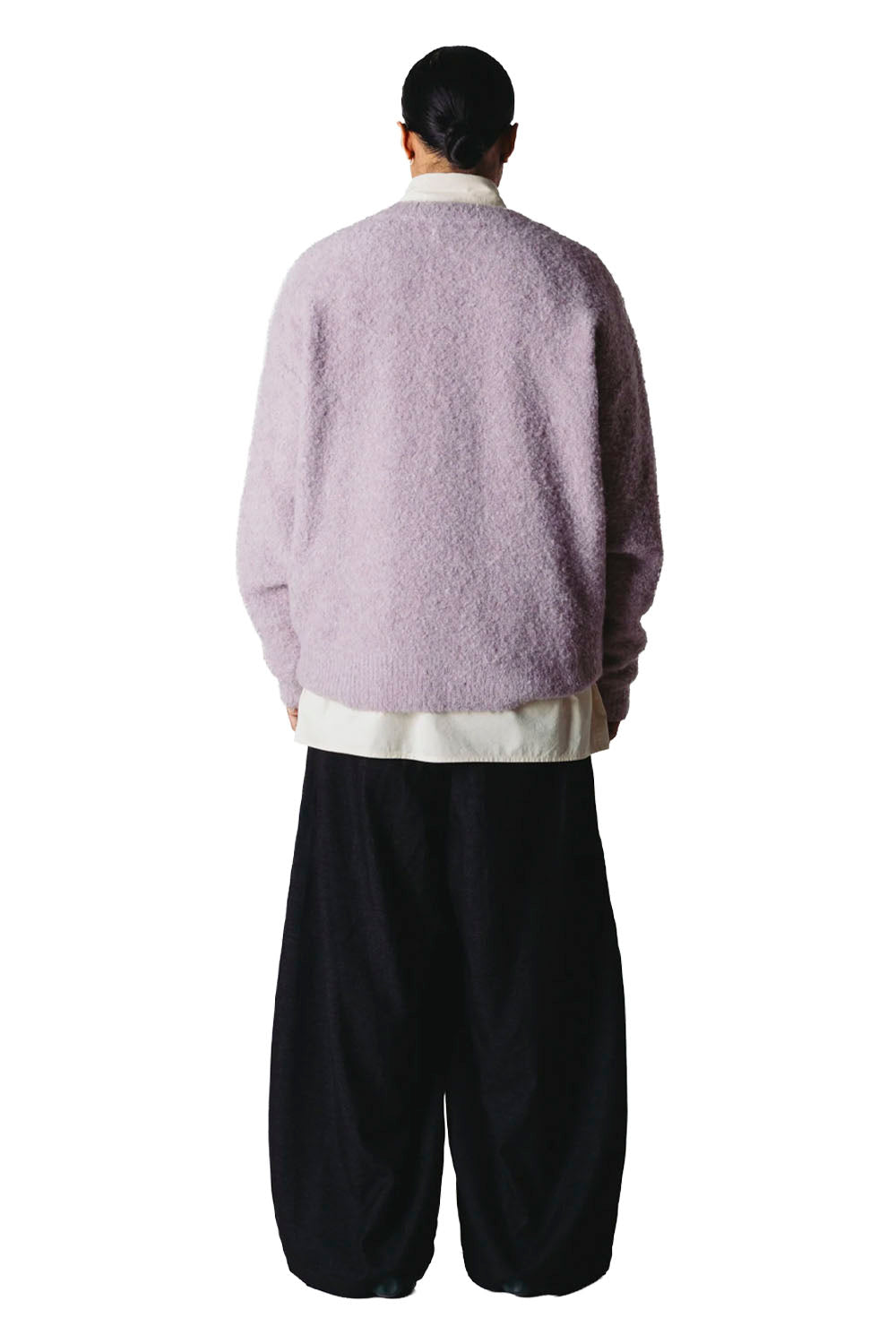 A person shown from the back wearing a fuzzy light lavender cardigan over a cream shirt and loose black pants, photographed against a plain white studio background.