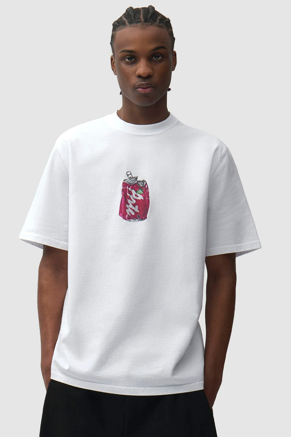 A model wearing a white short-sleeve crewneck t-shirt with a small red and white graphic of a soda can on the center chest, paired with black pants, against a light gray background.