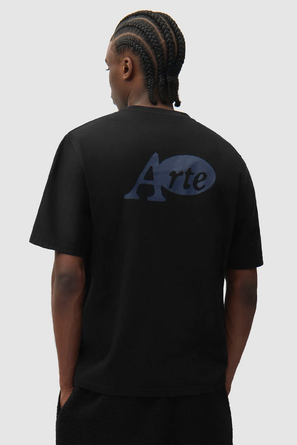 A man viewed from behind wearing a black short-sleeve t-shirt with a dark blue 'Arte' logo printed on the back, set against a solid light gray background.