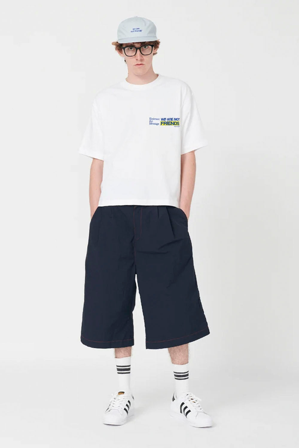 Person wearing a white t-shirt with text, navy blue pants, and white sneakers on a white background