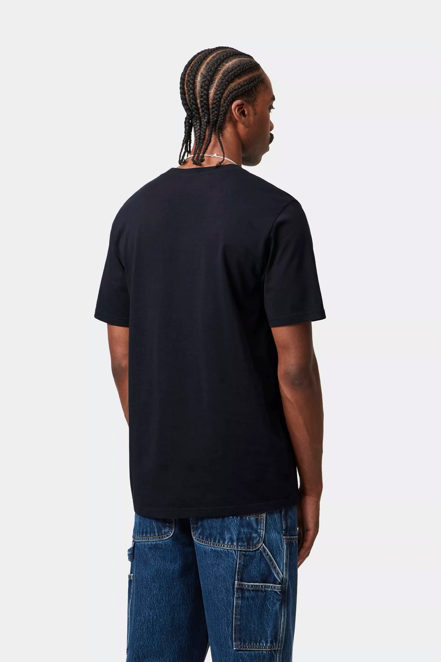 Man wearing a navy Carhartt Pocket t-shirt  and blue jeans on a white background