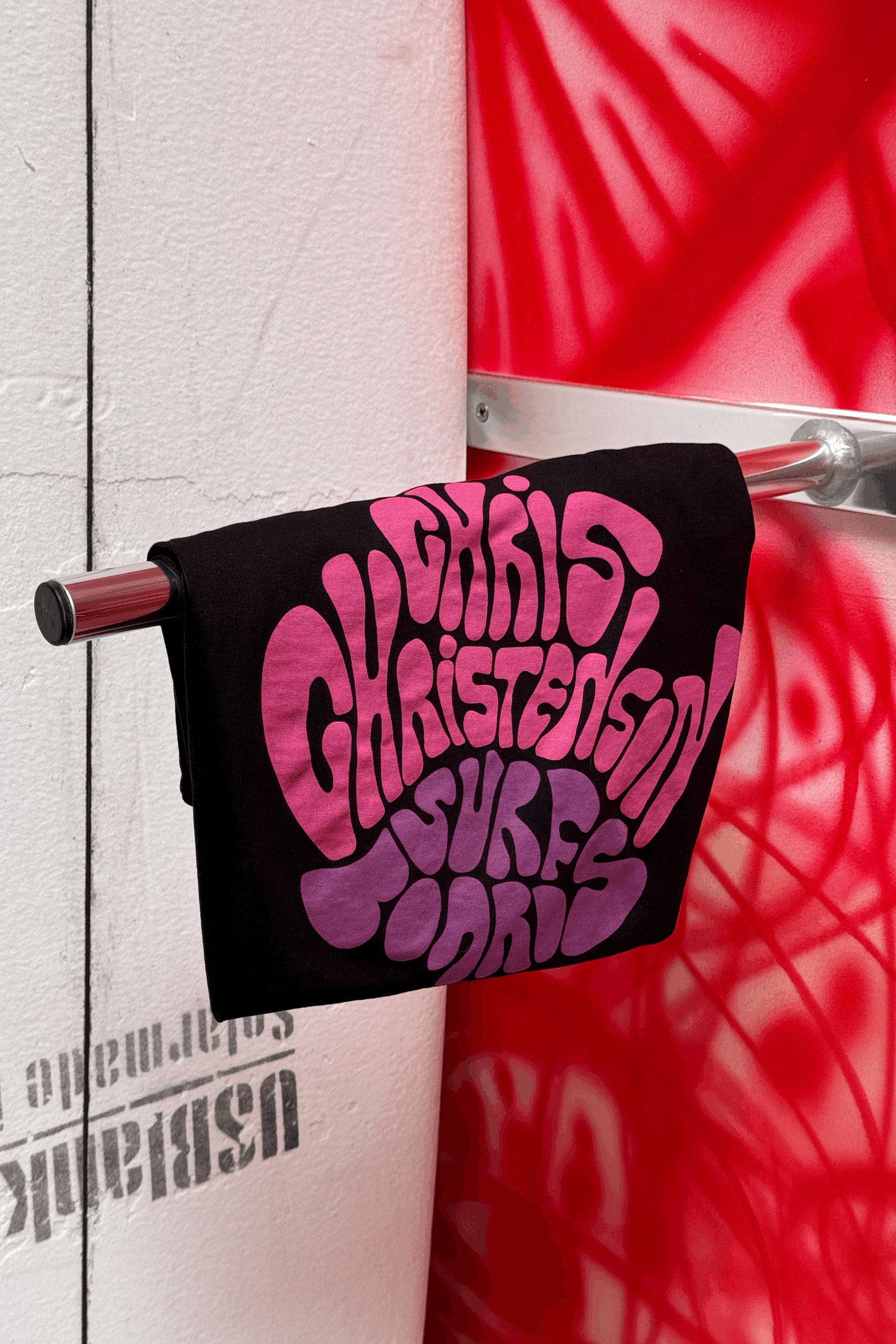 Christenson Black tee with pink text hanging on a rack Pukas Surf Shop
