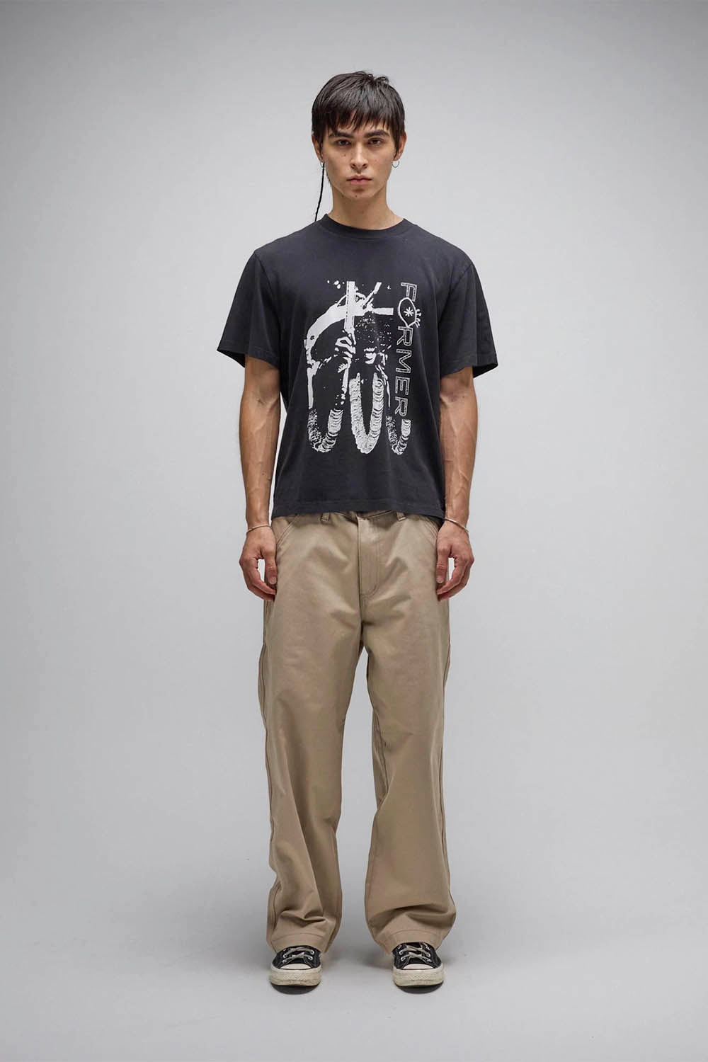 Person wearing a black t-shirt with graphic design and beige pants on a gray background