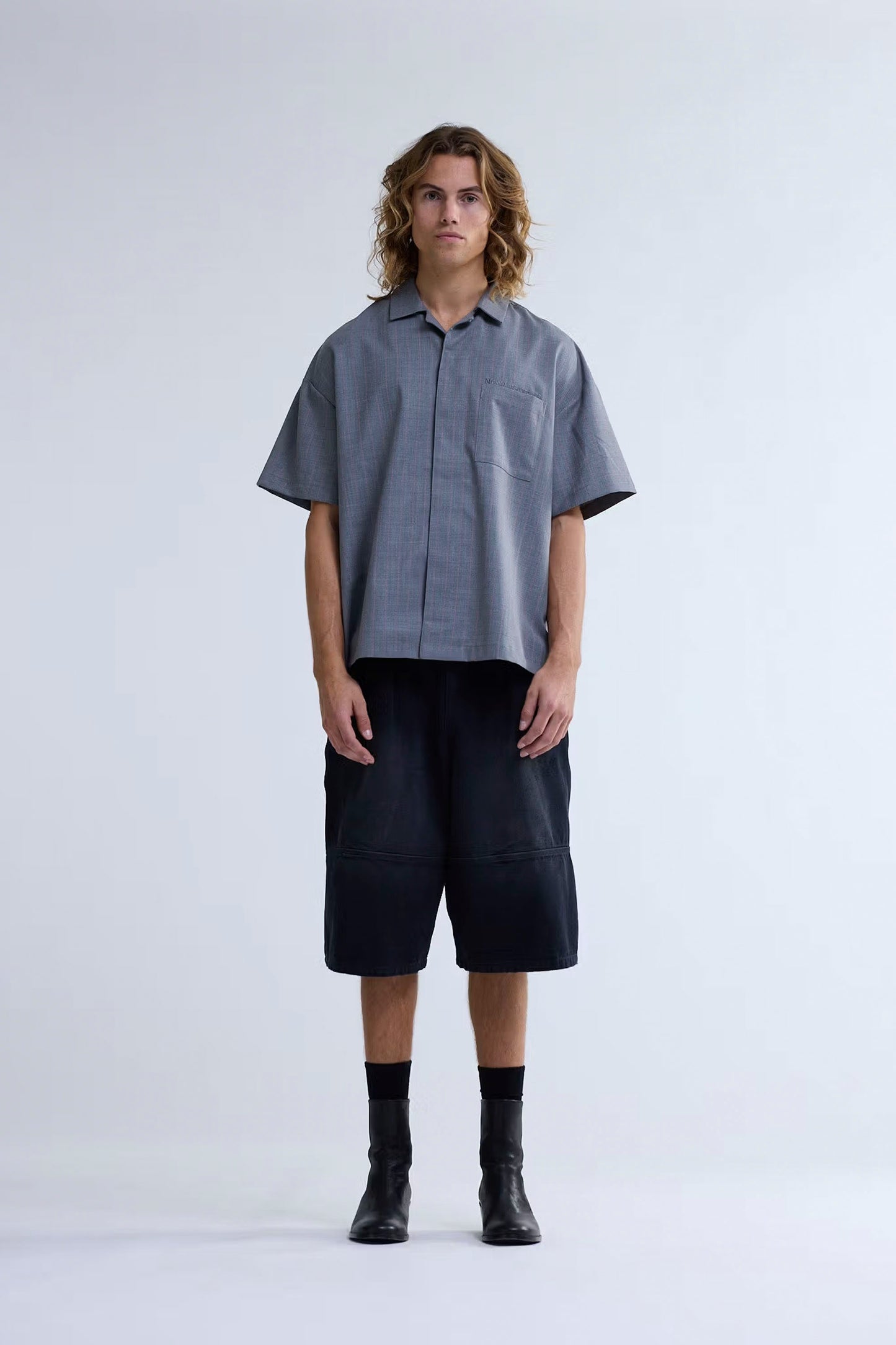 Person wearing a gray short-sleeve shirt and black shorts on a white background