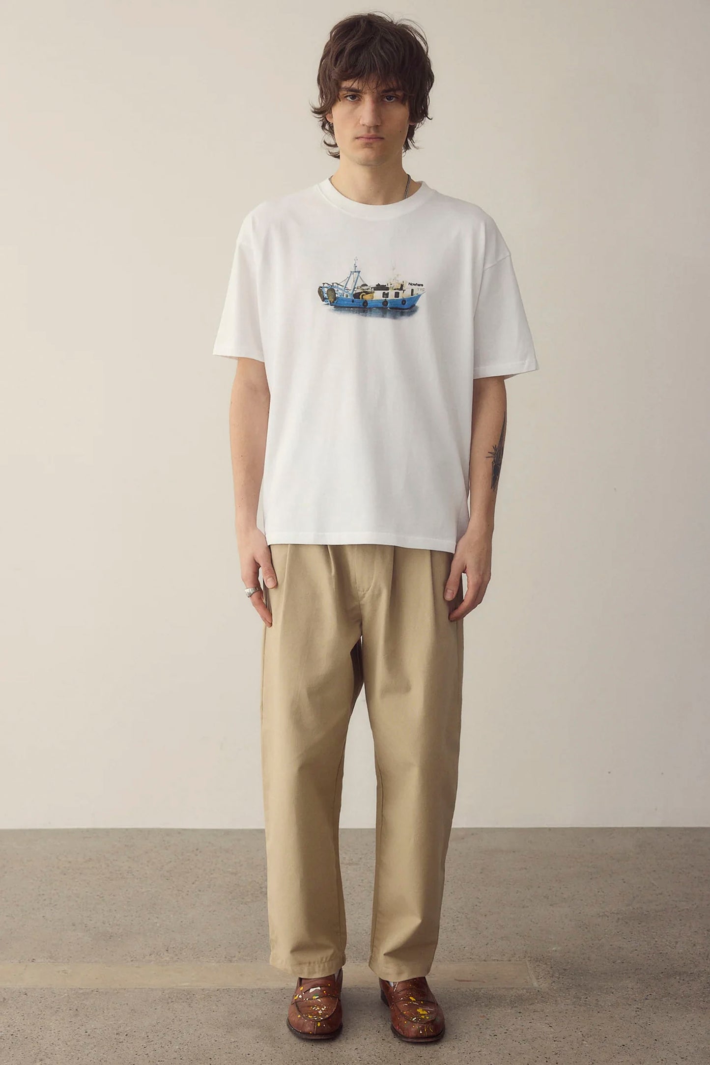 Person wearing a white NWHR t-shirt with a graphic design and beige pants against a plain background