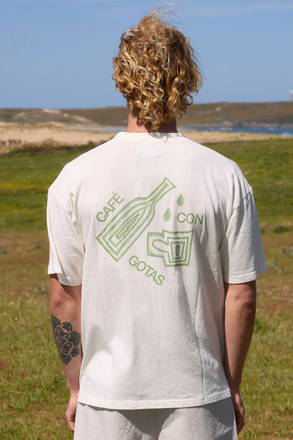 Person wearing a white t-shirt with green graphics and text in an outdoor setting
