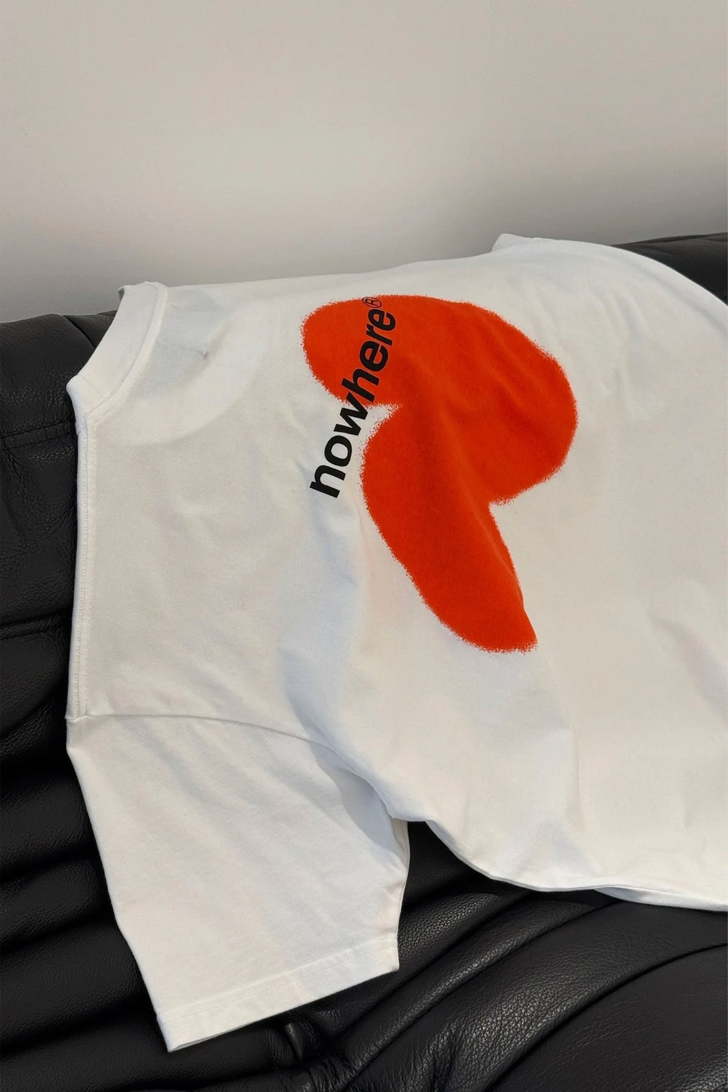White NWHR t-shirt with red circle and text 'nowhere' on a black surface