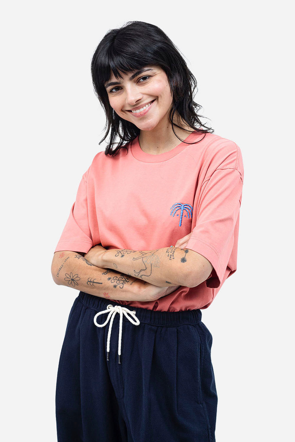 Woman wearing a pink t-shirt with a palm tree design and dark pants on a white background